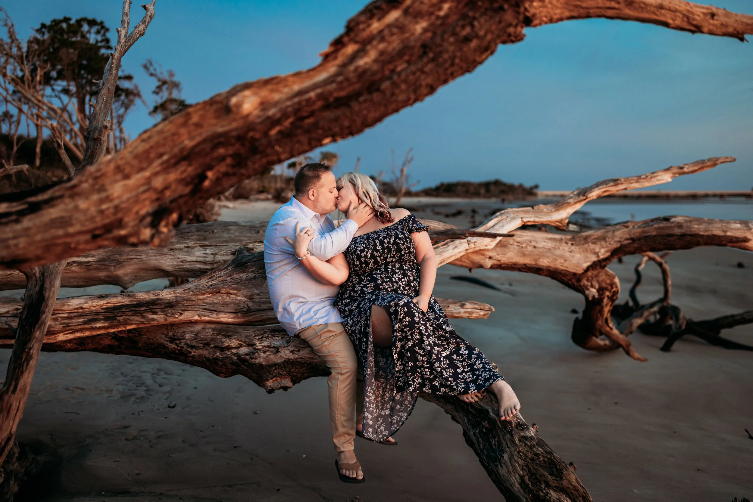 Couple kissing on driftwood at sunrise during romantic beach session at Boneyard Beach Big Talbot Island in Jacksonville Florida