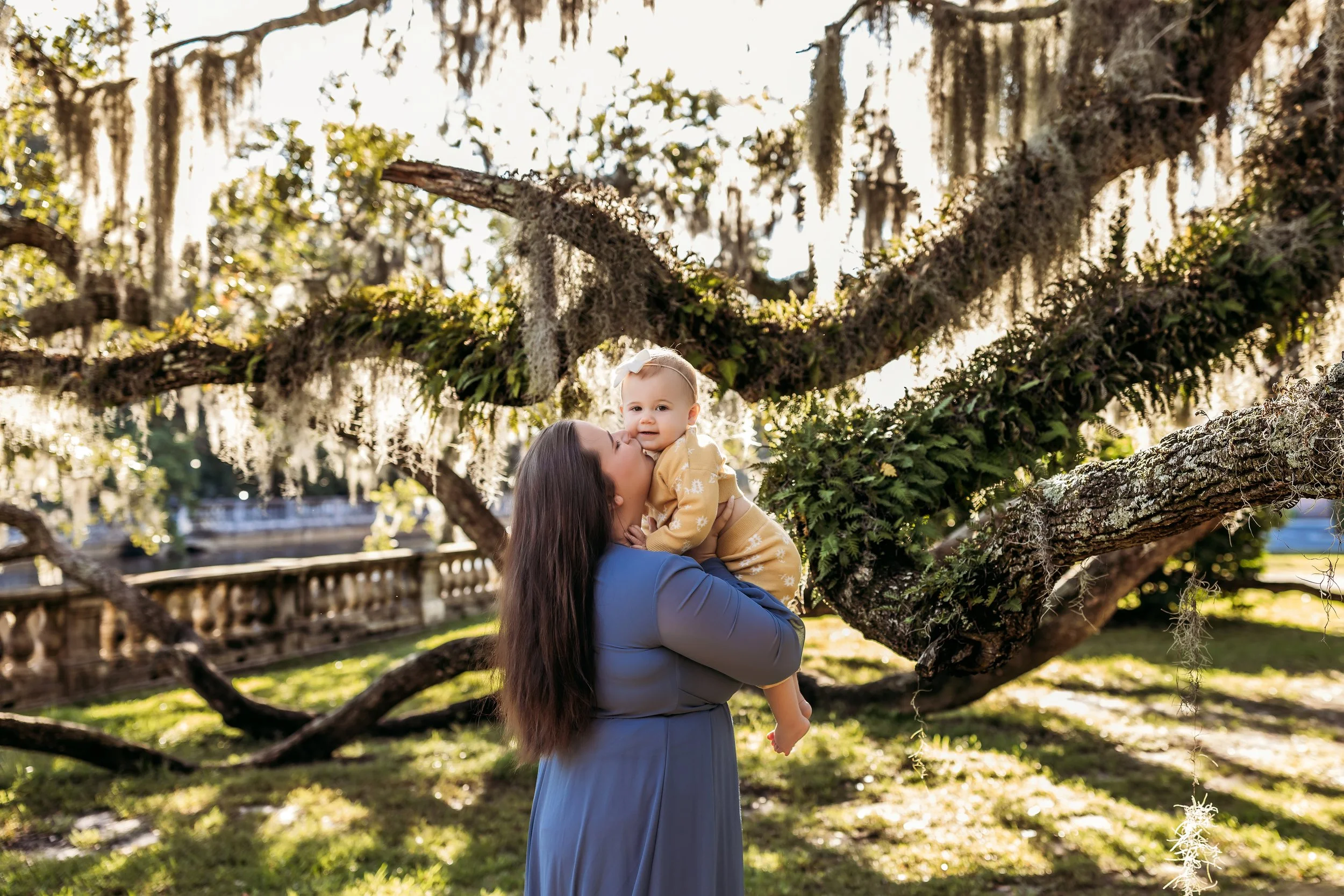 Mother holding baby under oak trees with Spanish moss during mommy and me session in Riverside Jacksonville Florida
