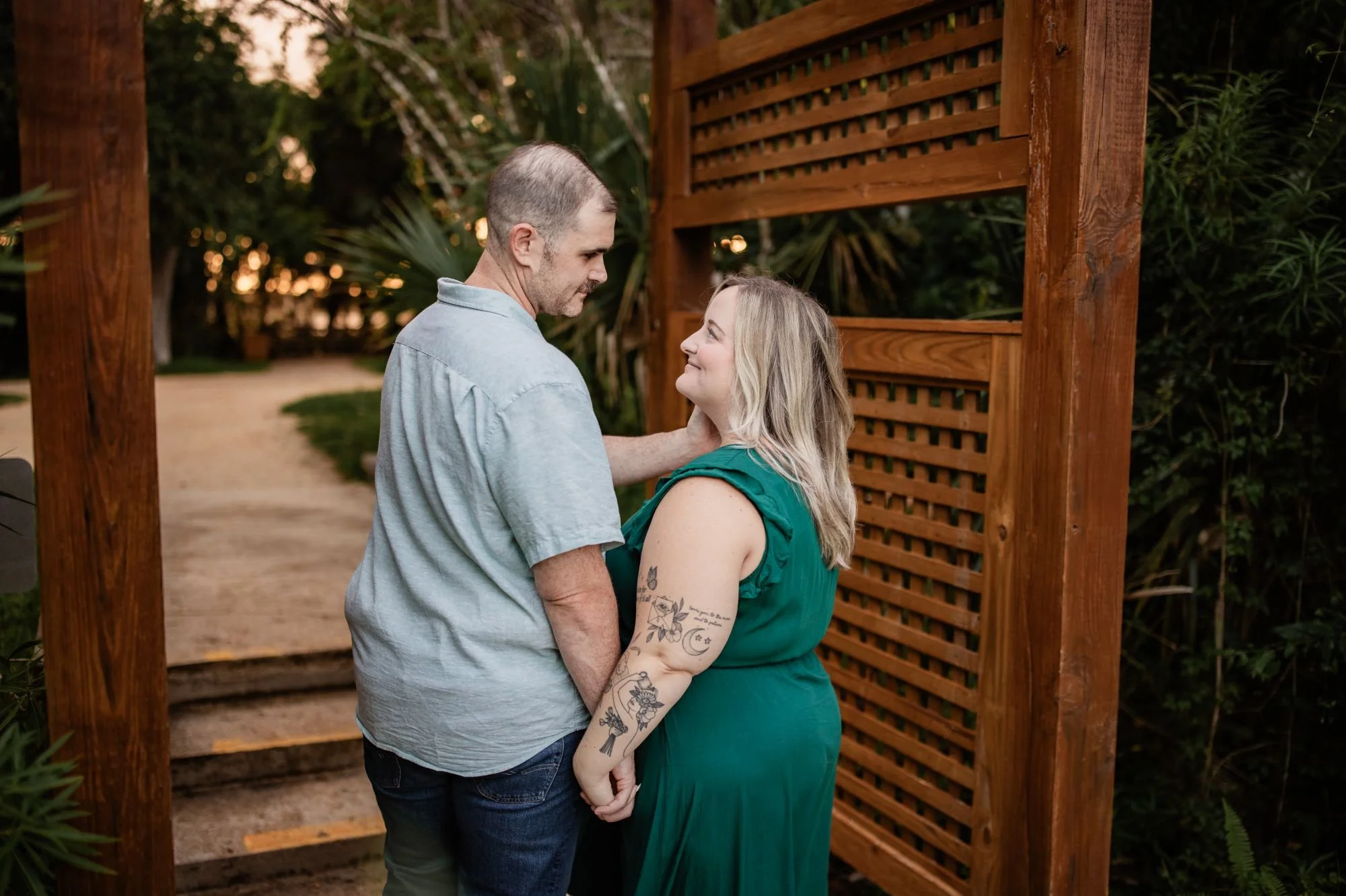Engaged couple holding hands and looking at each other beside a wooden garden structure at Washington Oaks.