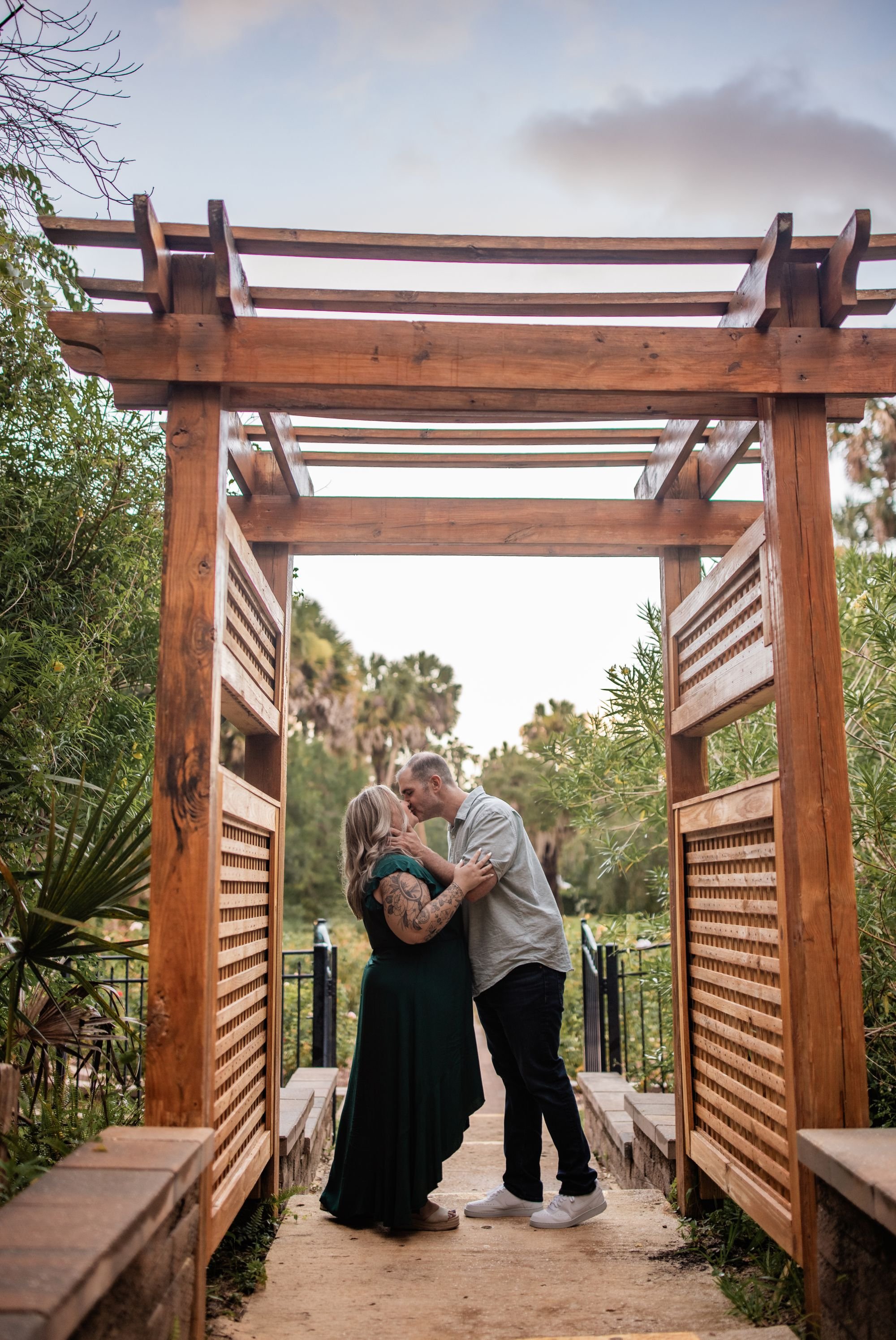 Couple kissing beneath a wooden garden arbor during their Washington Oaks engagement session.