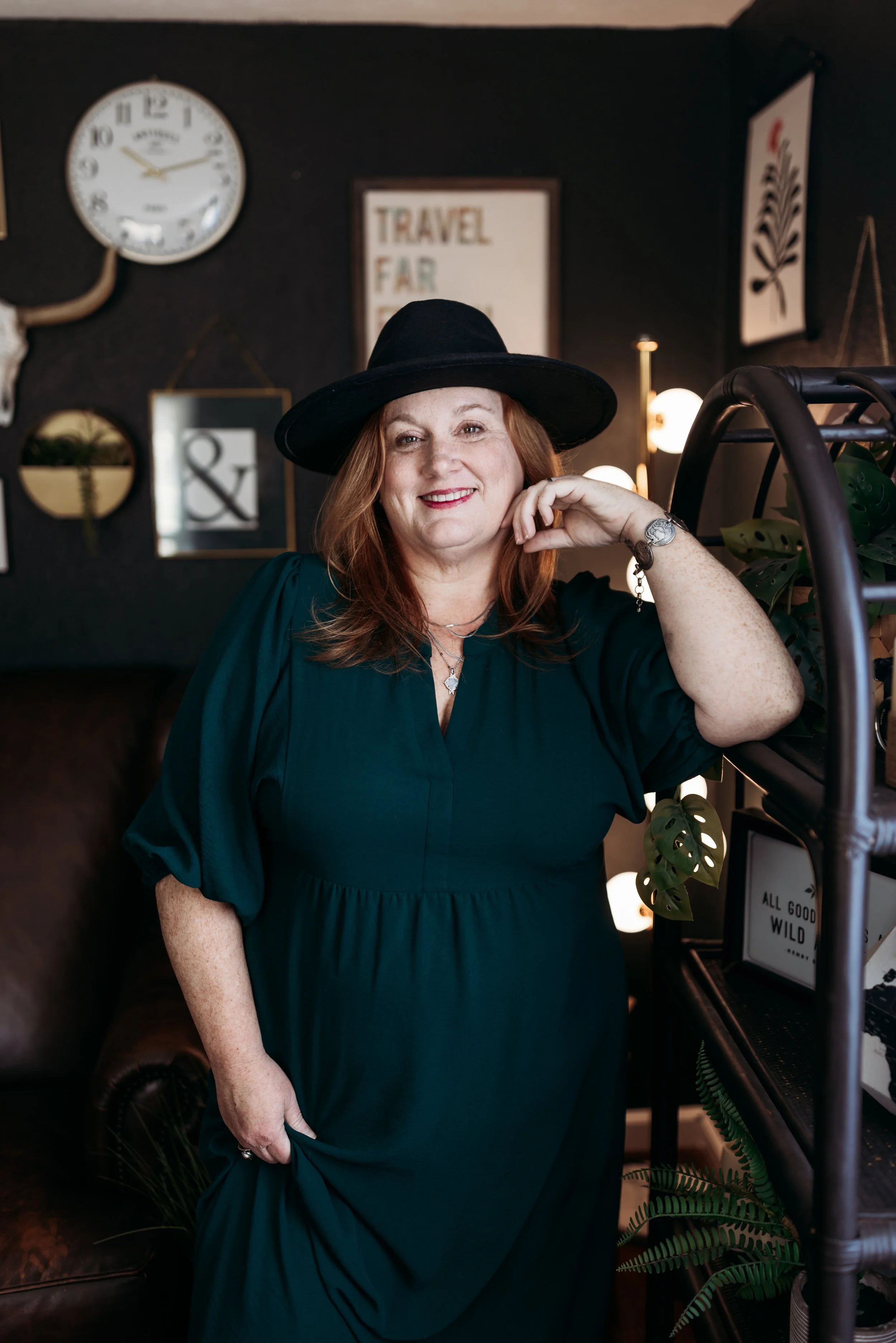 Woman in a green dress and black hat smiling in a cozy studio space, photographed for a Jacksonville branding headshot