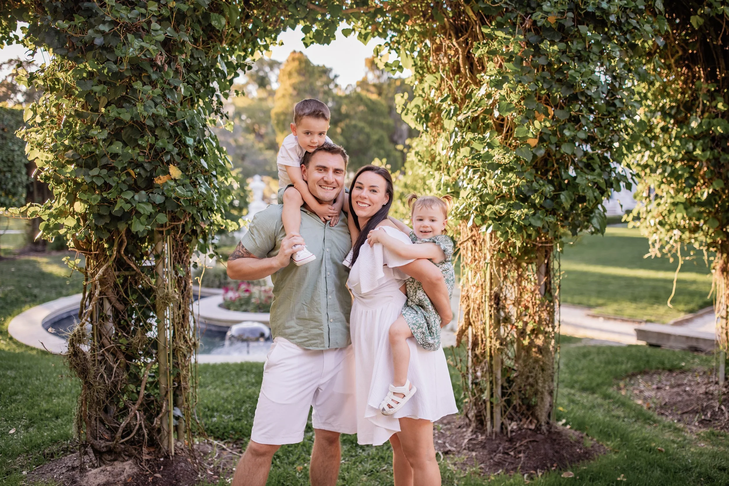 Family of four smiling together under greenery arch during golden hour session on Jekyll Island