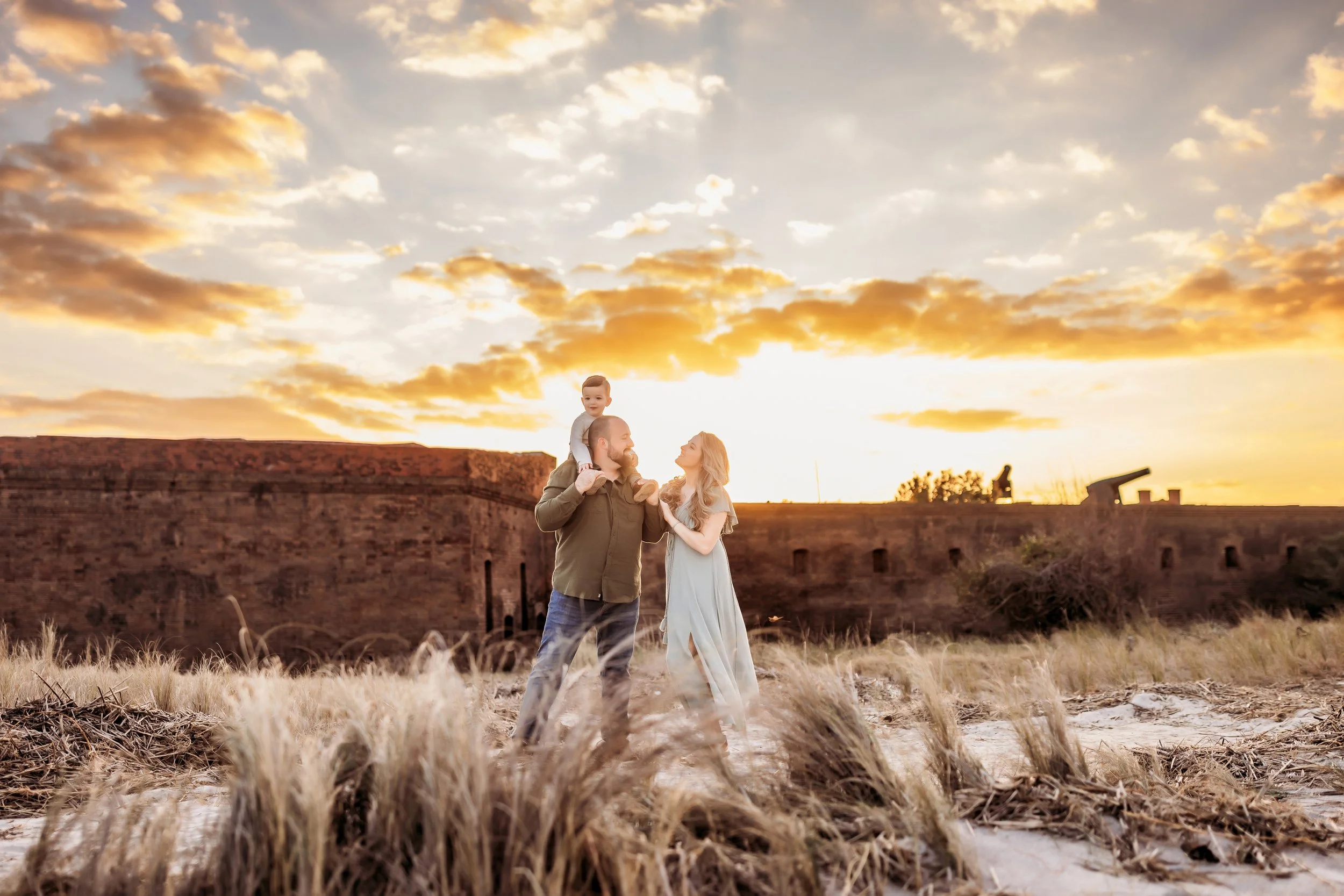 Family walking together at sunset at Fort Clinch in Fernandina Beach, Florida, with a young child on a parent’s shoulders during a golden hour family photography session
