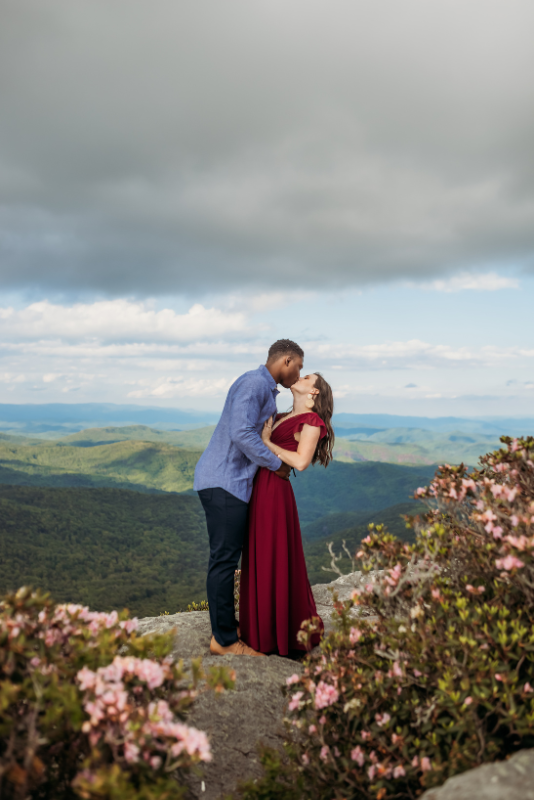 Couple kissing at a mountain overlook in coordinated burgundy and blue jewel tones