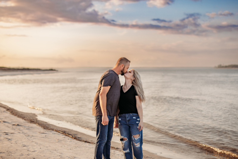 Couple kissing at the shoreline in casual black tops and denim at sunset