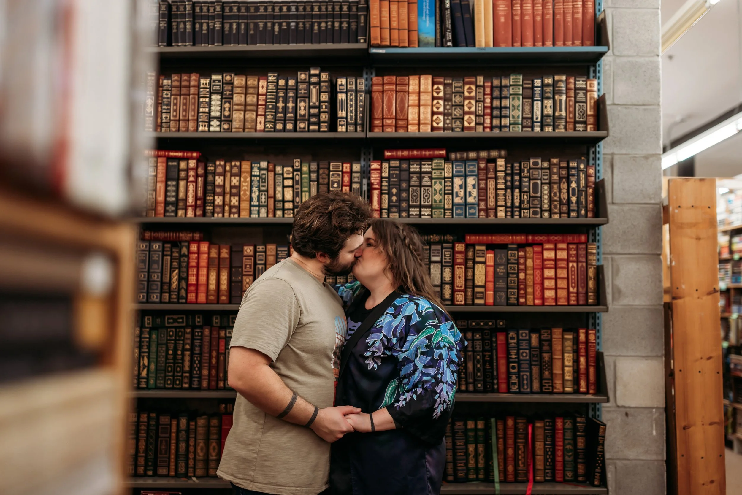 Couple kissing in front of vintage bookshelves during romantic session at Chamblin’s Book Mine in downtown Jacksonville