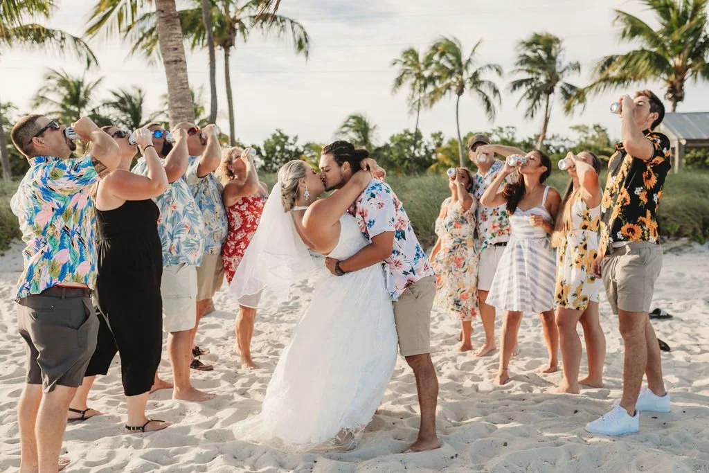 Newlyweds kissing on a Key West beach while their wedding guests celebrate around them