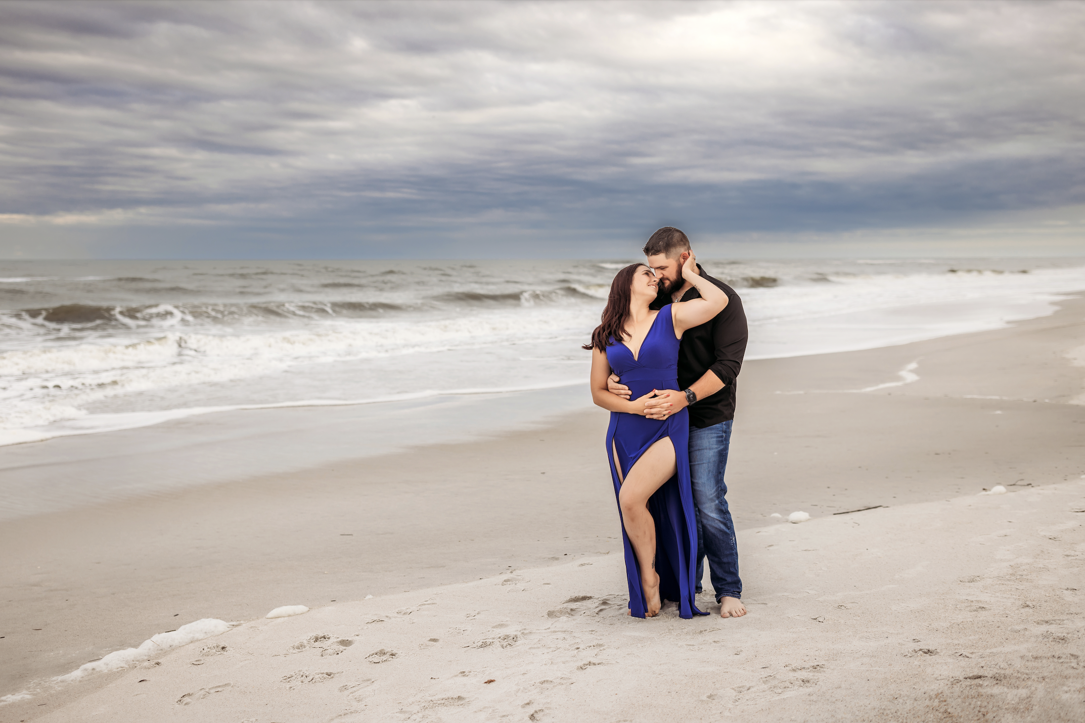 Couple standing on a dramatic beach in a royal blue dress and black shirt