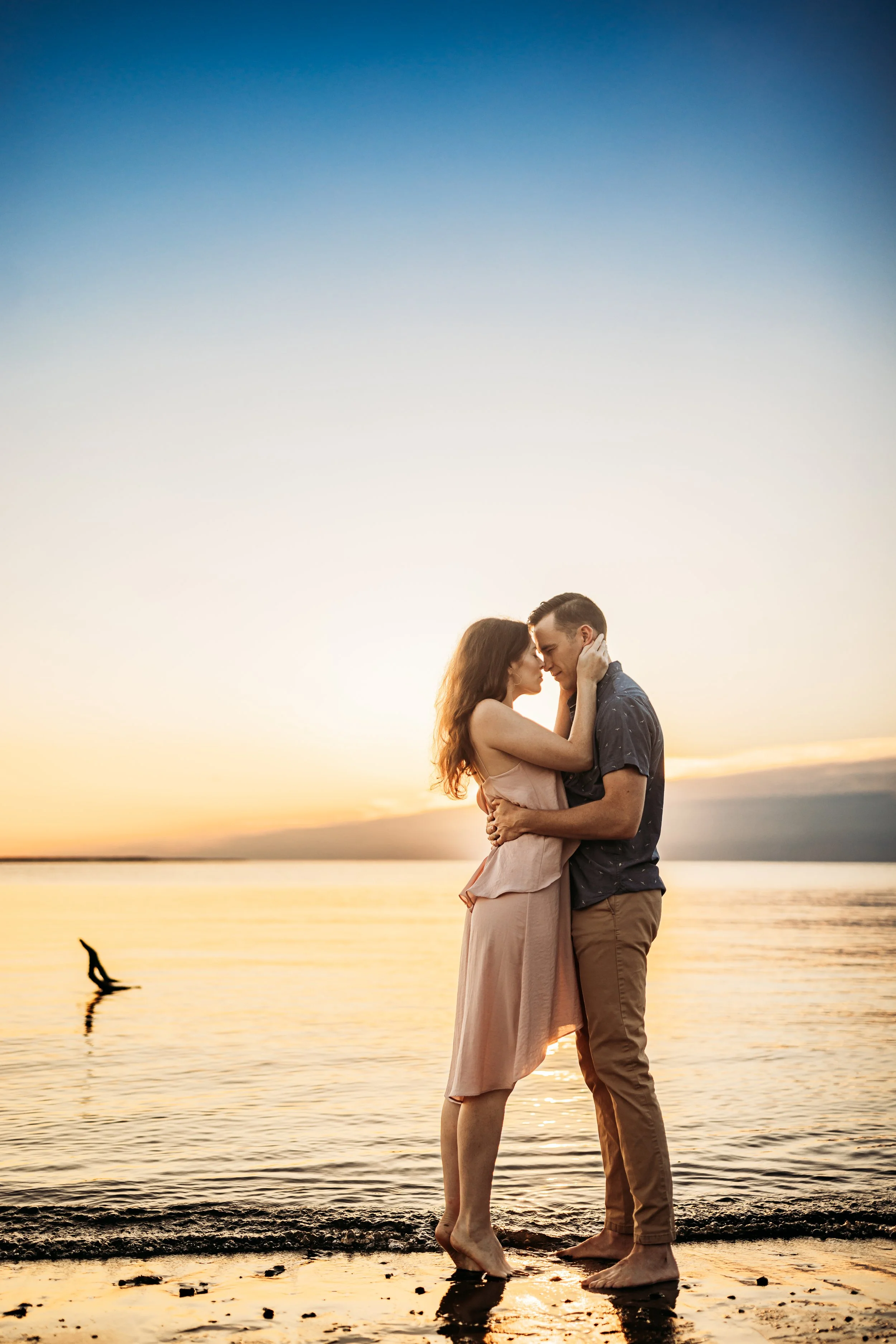 Couple kissing barefoot at sunset in a blush dress and navy shirt during a Florida beach session