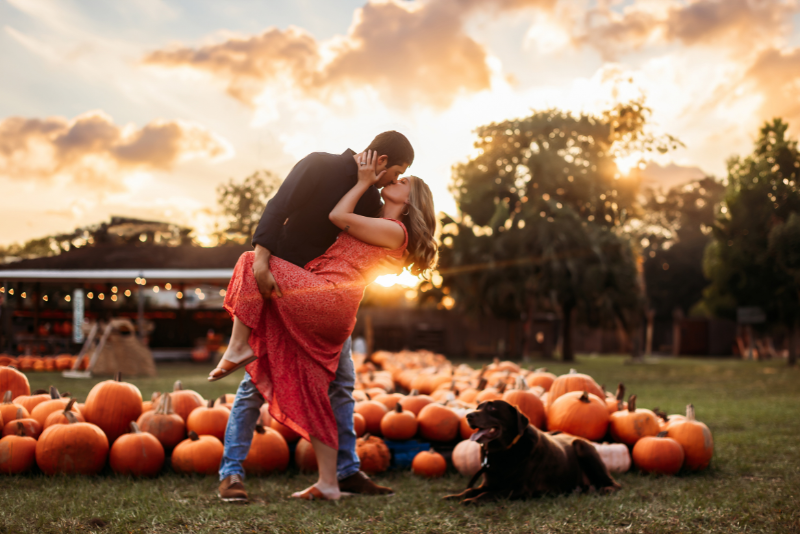 Couple with their dog at a pumpkin patch in coordinated coral, black, and denim outfits