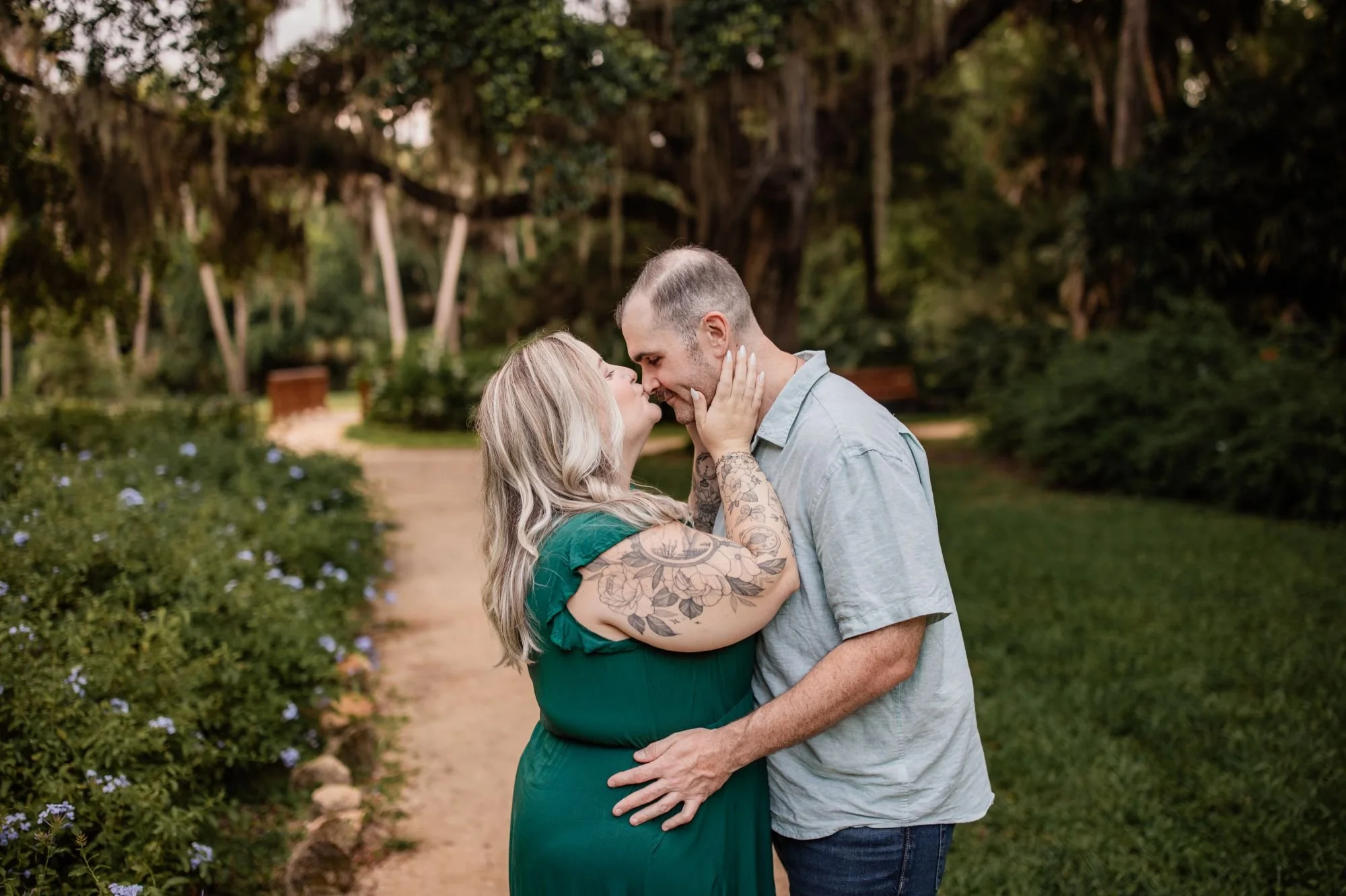 Couple leaning in for a kiss on a garden path beneath moss-covered oak trees at Washington Oaks.