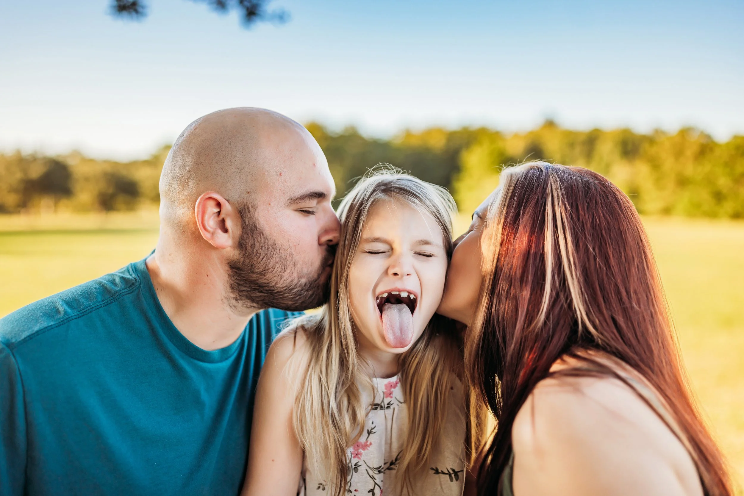 Parents kissing child on cheeks during playful family session at Camp Milton in West Jacksonville Florida