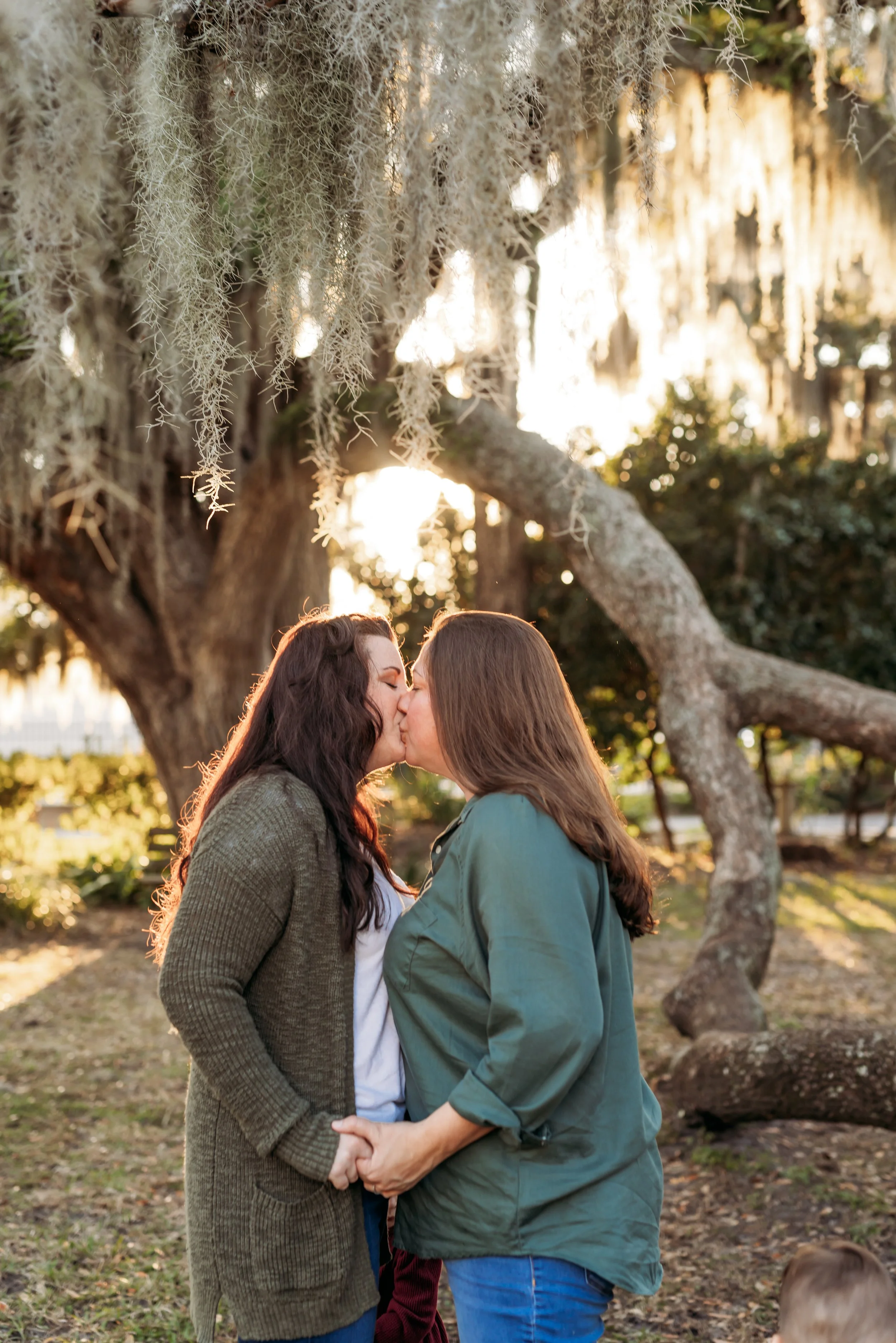 Lesbian moms kissing under oak trees during family session in Riverside Jacksonville Florida