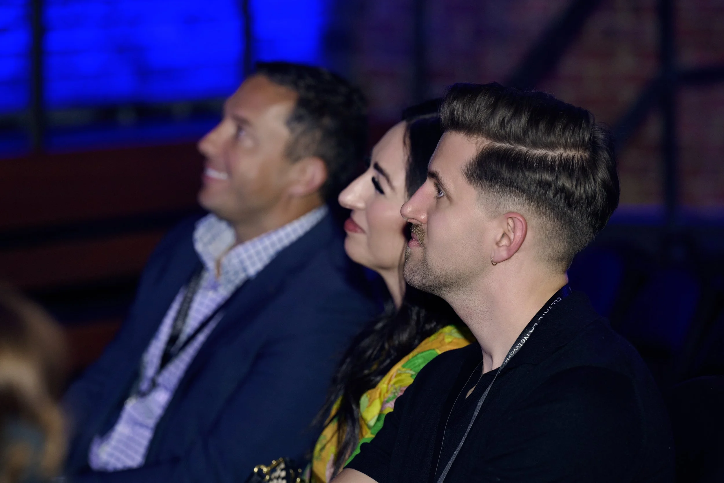 Three people sitting and watching an event, with a dark background and blue lighting.