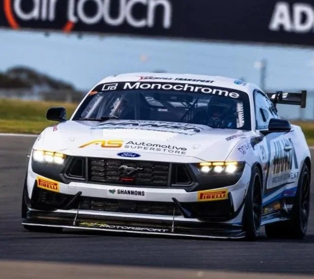 White race car on track with sponsor logos, moving at high speed, with a blurred background.