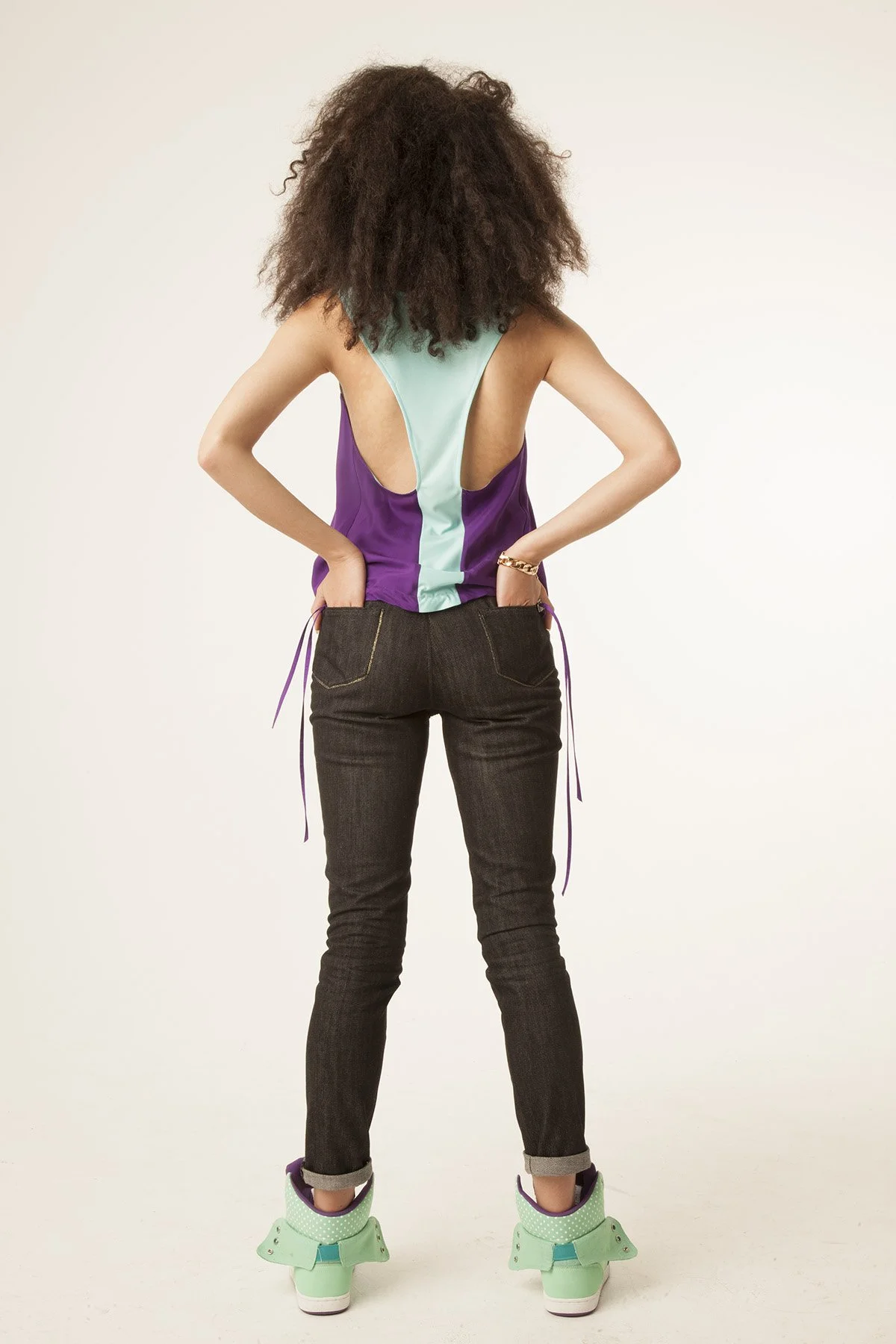 Person wearing green ice skates, dark jeans, and a colorful sleeveless top, standing with their back to the camera.