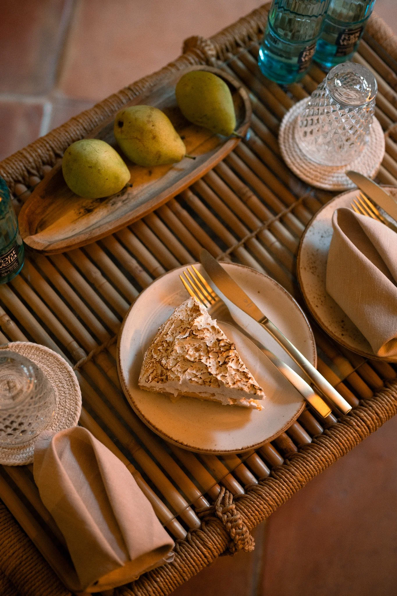 Pears, cake and tableware arranged on a wicker table in warm afternoon light at La Residencia.