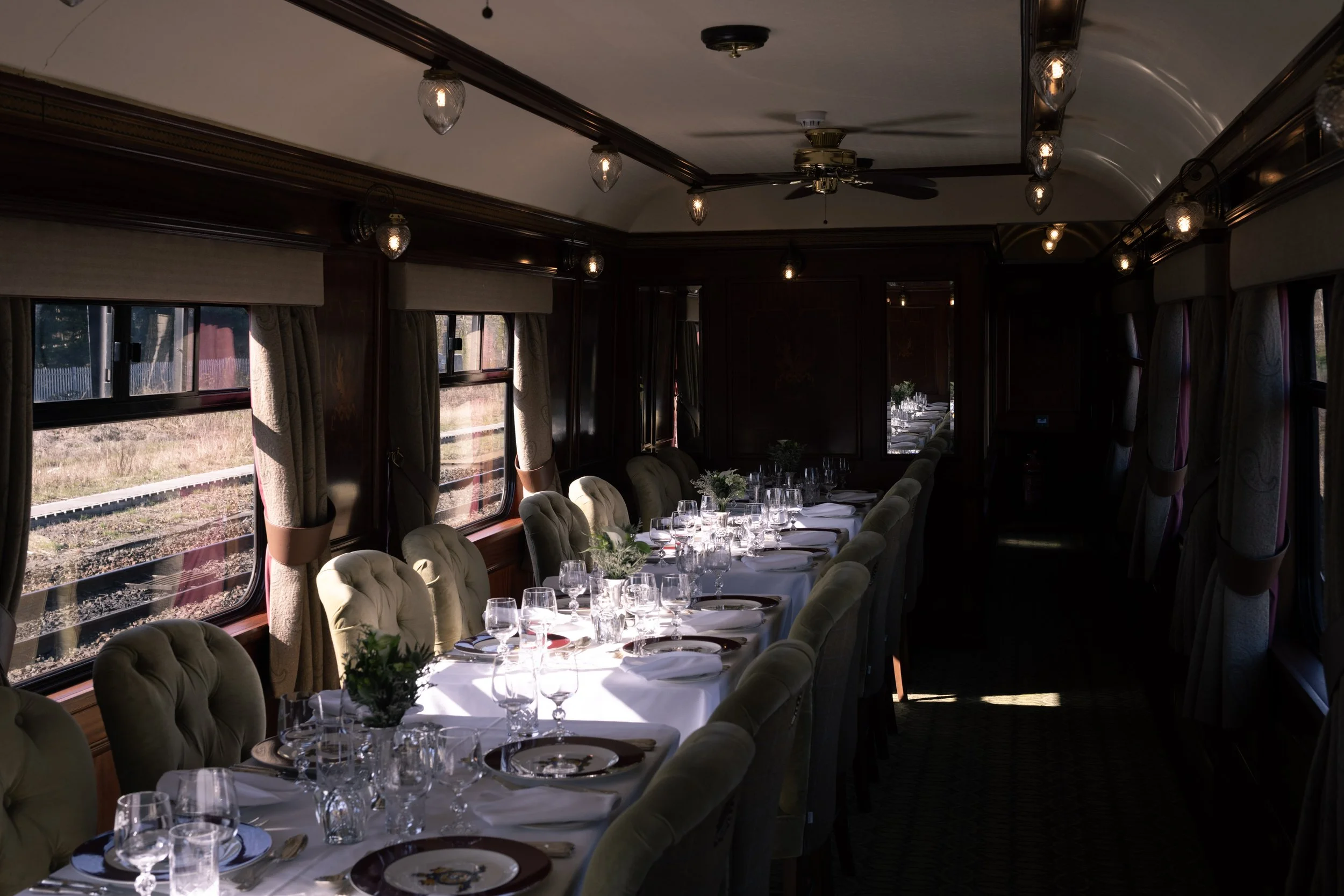 Inside a vintage train dining car with a long table set with white tablecloths, glassware, and floral centerpieces.