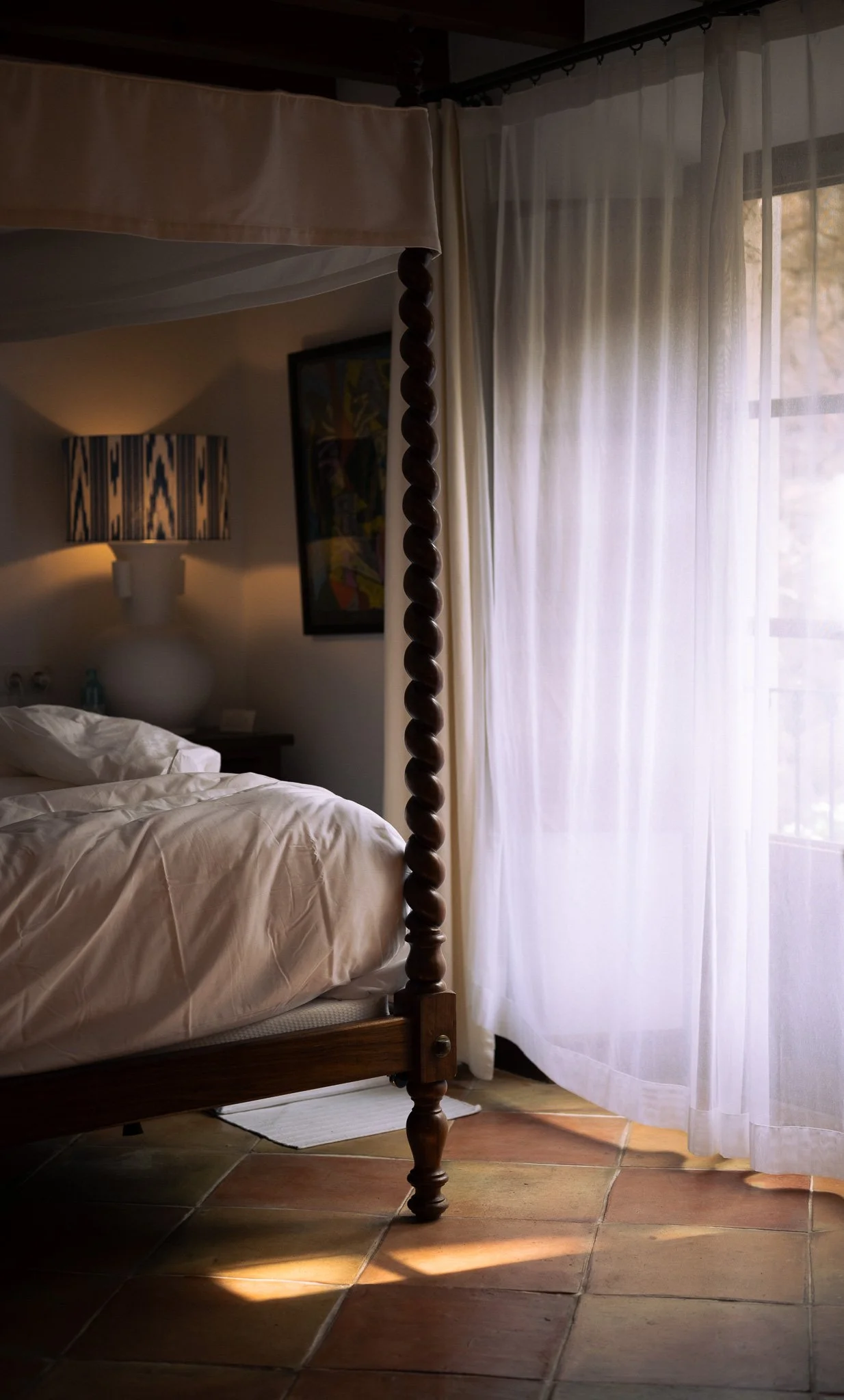 Four-poster bed and sheer white curtains illuminated by soft window light at La Residencia in Mallorca.
