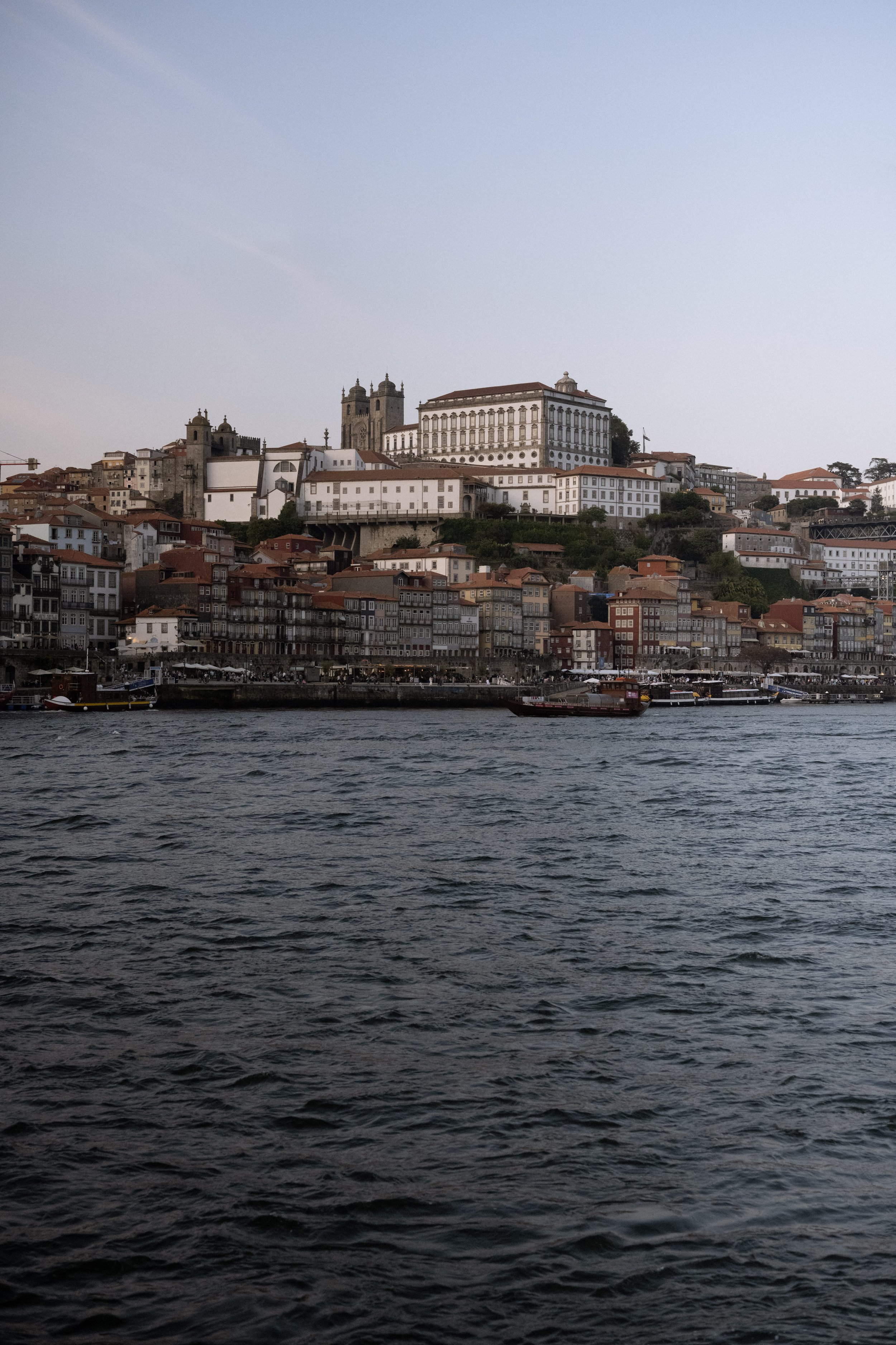 View of Porto, Portugal, with buildings on a hillside and boats on the river in the foreground.