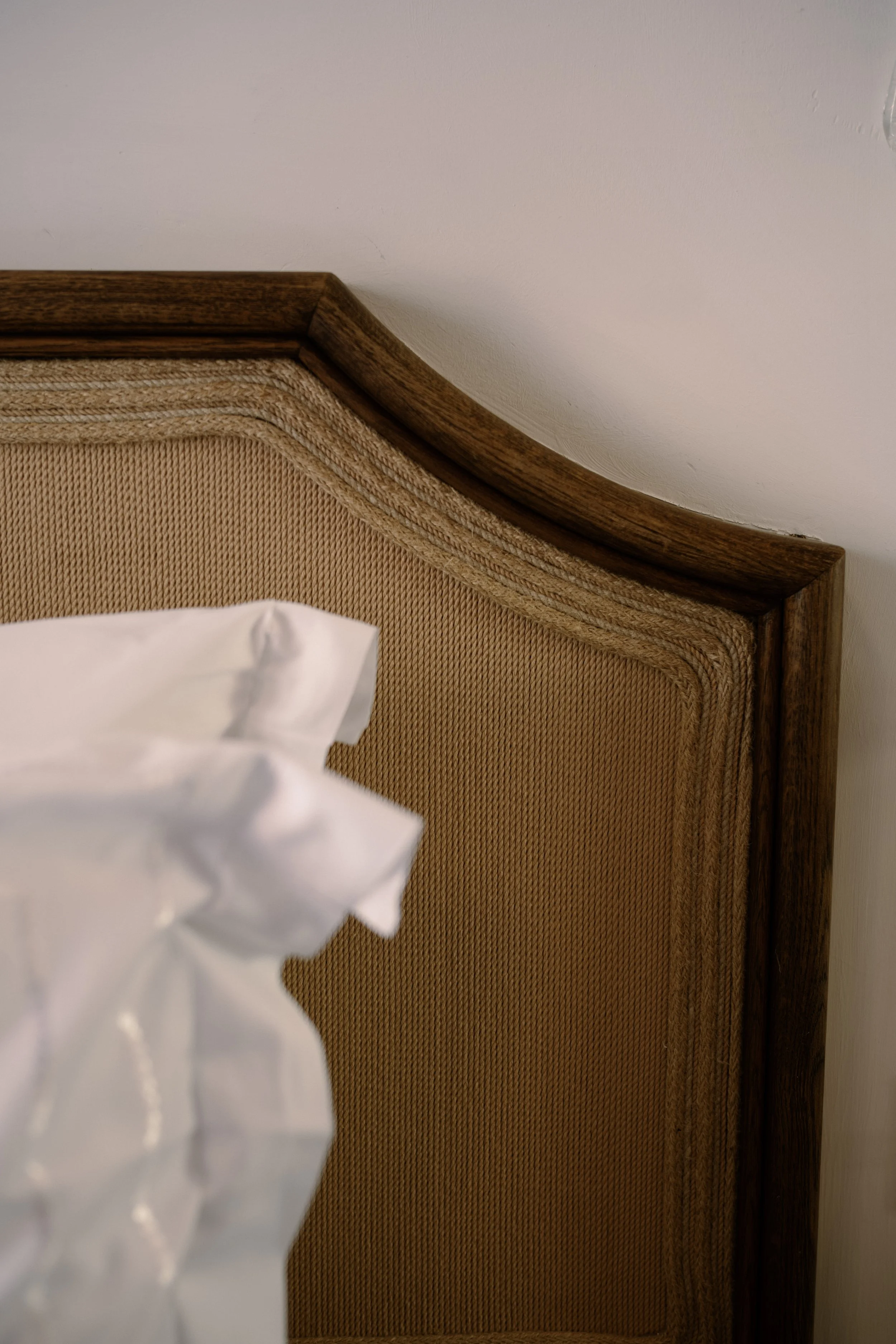 Close-up of a wooden headboard with textured fabric panel, part of a white pillow and bedding in the foreground.