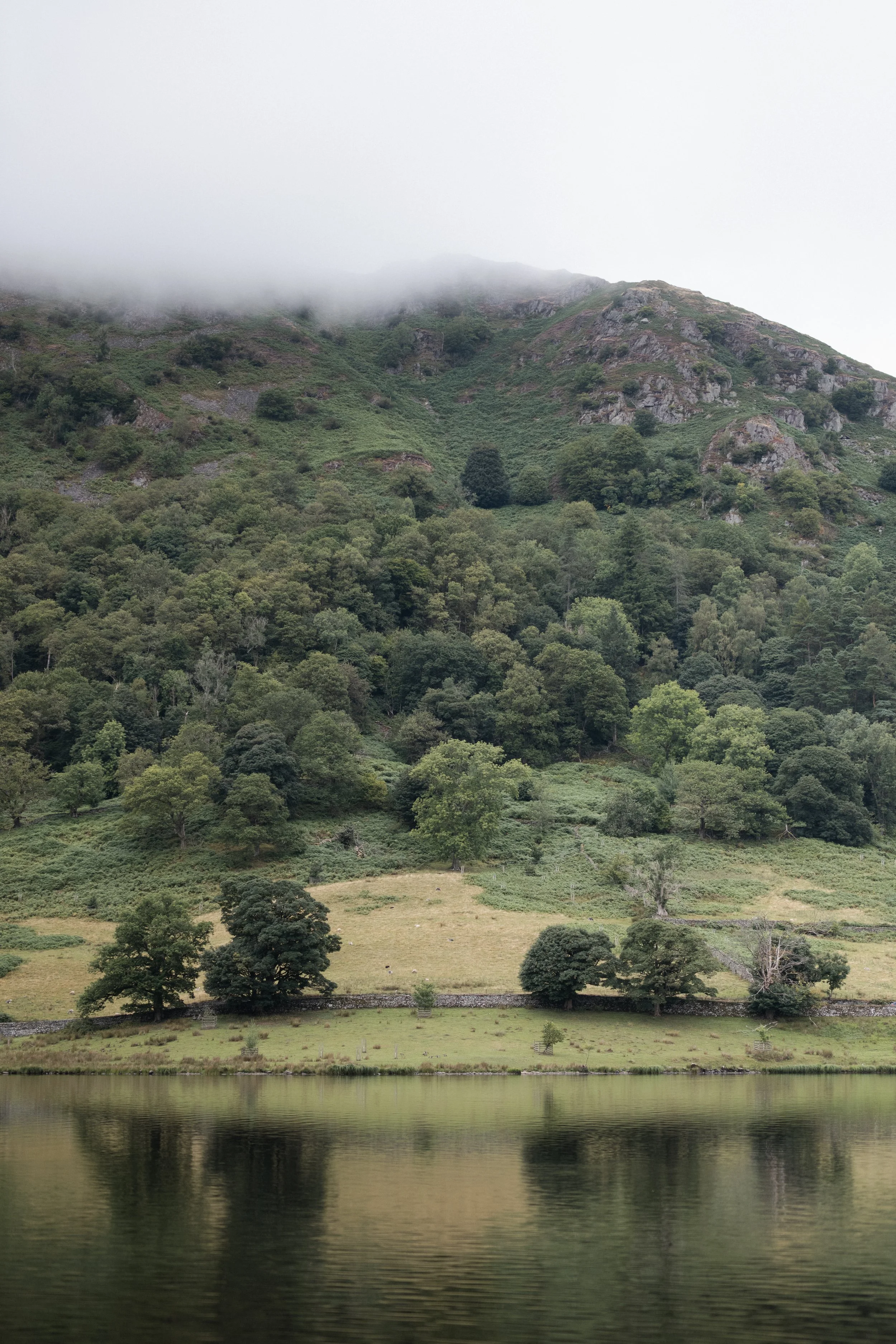 Mist-covered Lake District fells rising beyond green countryside near Windermere.