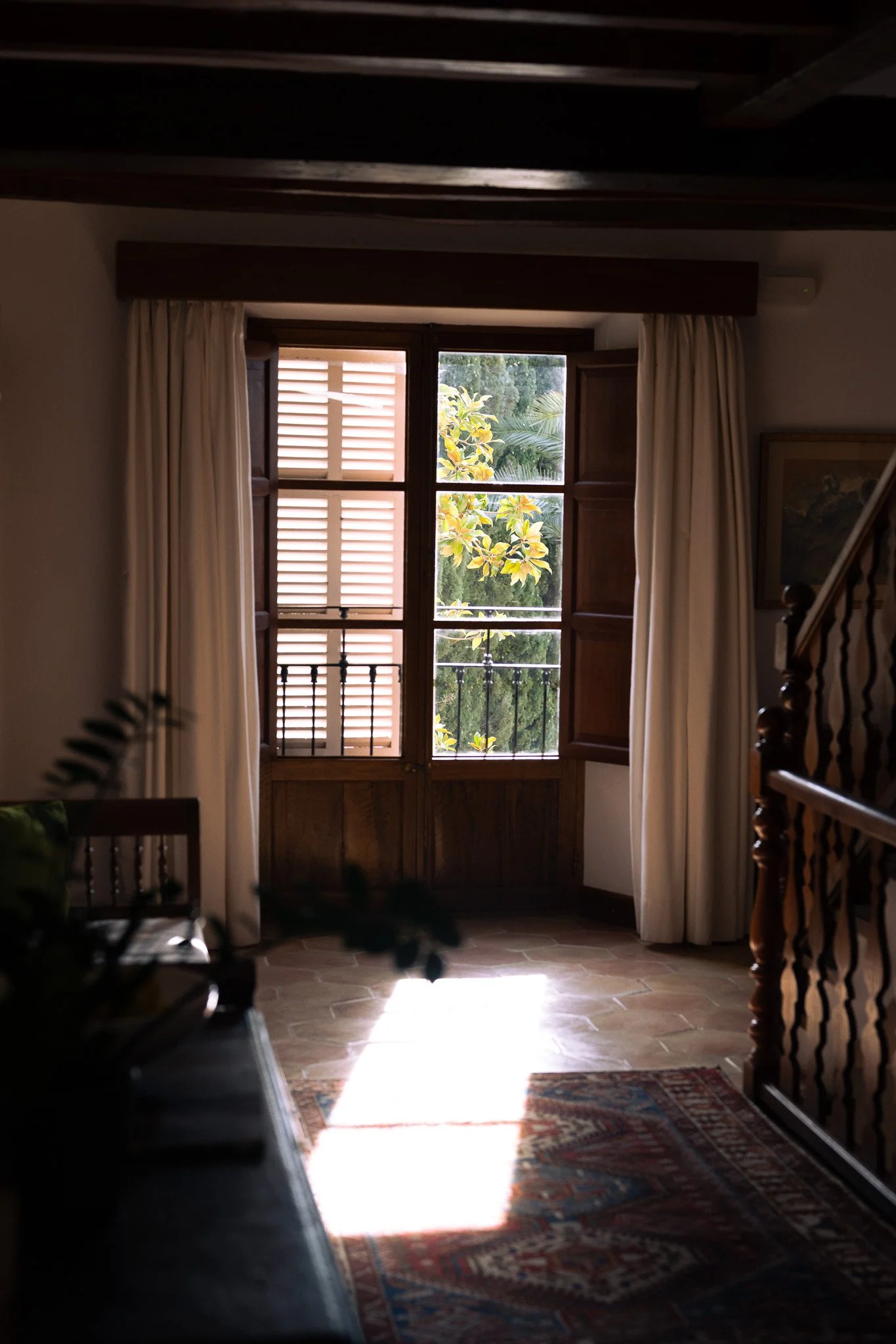 Sunlight falling through wooden shutters onto a patterned rug inside La Residencia in Deià.