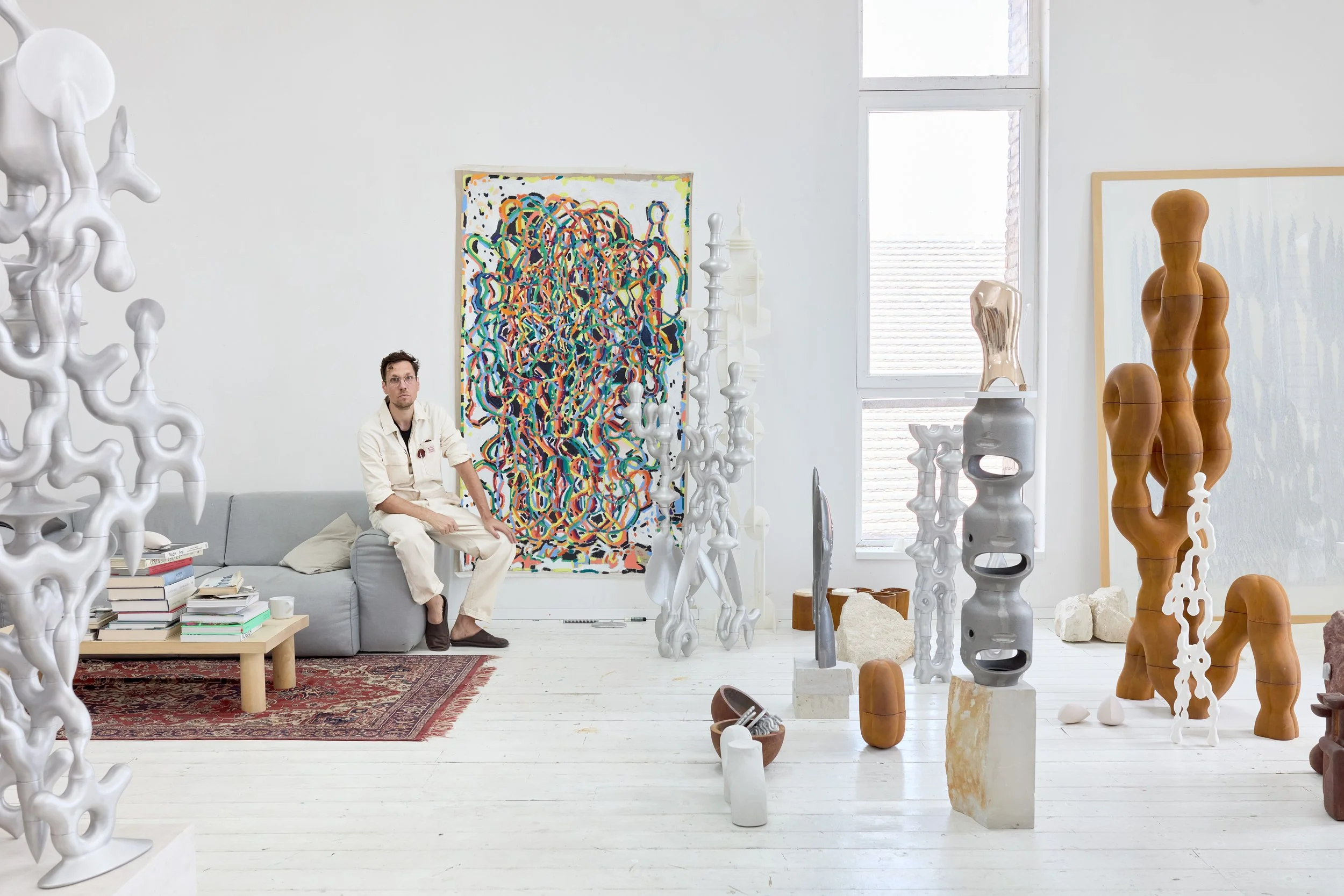 Sculptor Tamas Melkovics in his bright art studio, surrounded by abstract aluminum, terracotta, and bronze biomorphic sculptures and a large colorful painting.