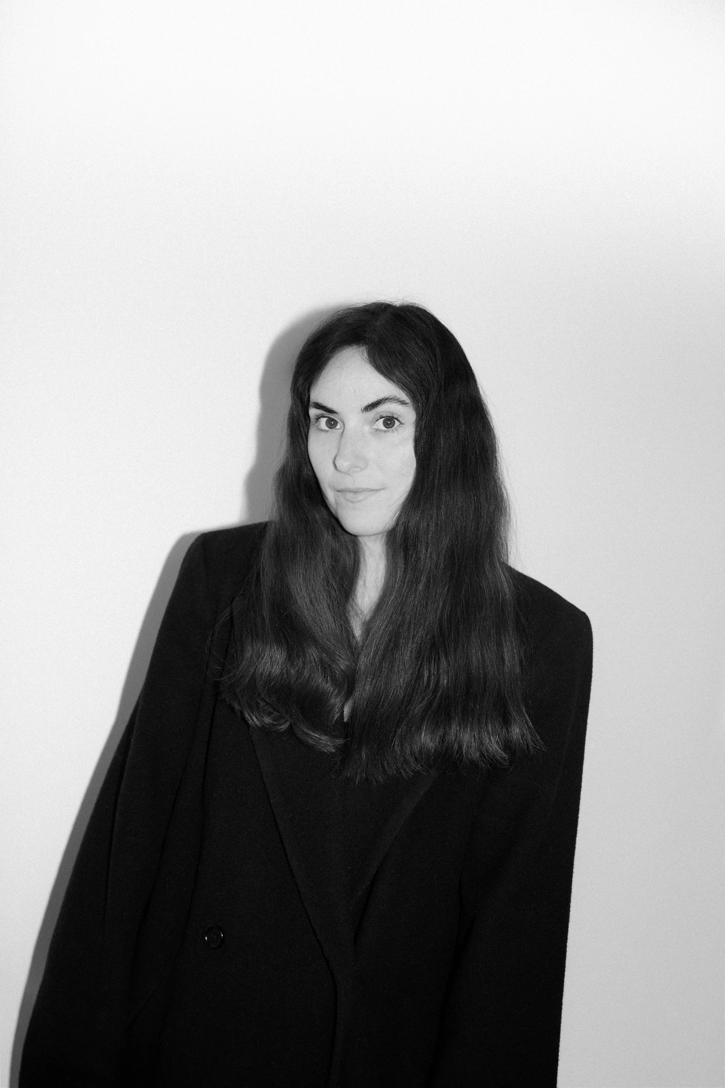 Black and white portrait of a woman with long dark hair, wearing a black coat, who is a Chicago and Edinburgh Wedding Photographer, named Melody Joy.