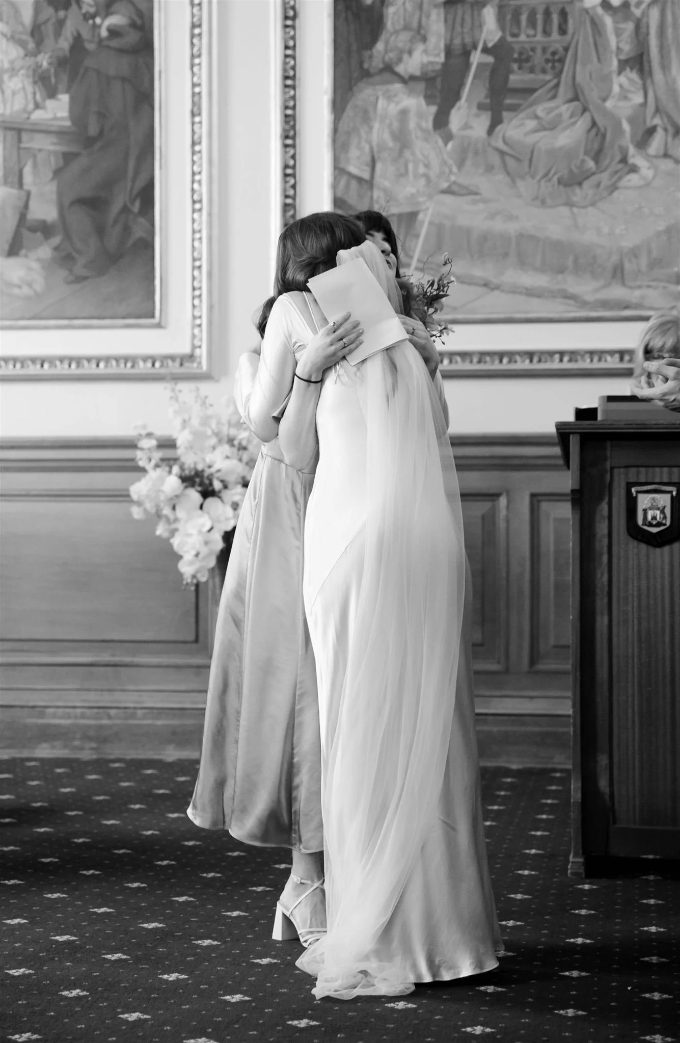 Bride hugging a bridesmaid inside Edinburgh City Chambers on their wedding day in Edinburgh.