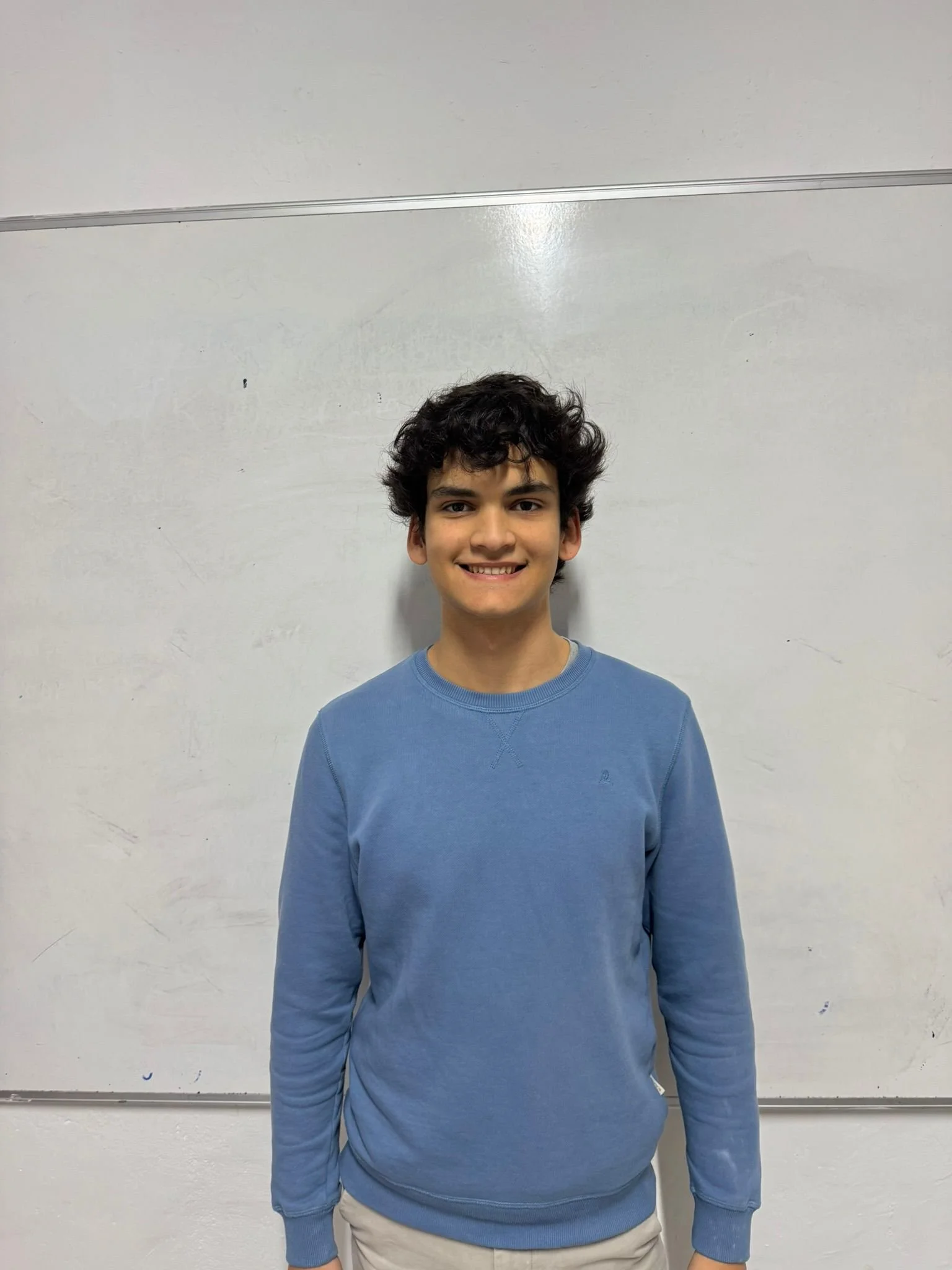 A man with curly black hair and a beard, wearing a white shirt, smiling and giving a thumbs-up, standing next to a woman holding a document.