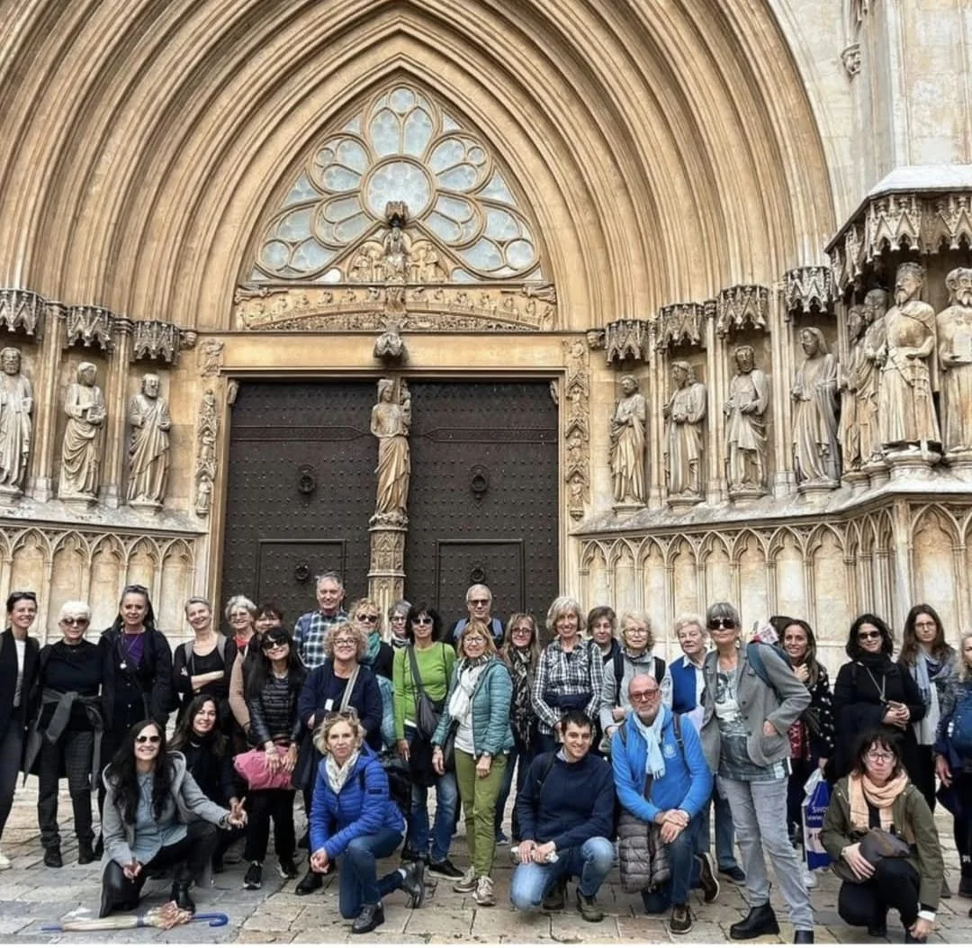 Group of tourists in front of an ornate Gothic cathedral entrance with detailed stone sculptures and a large wooden door.