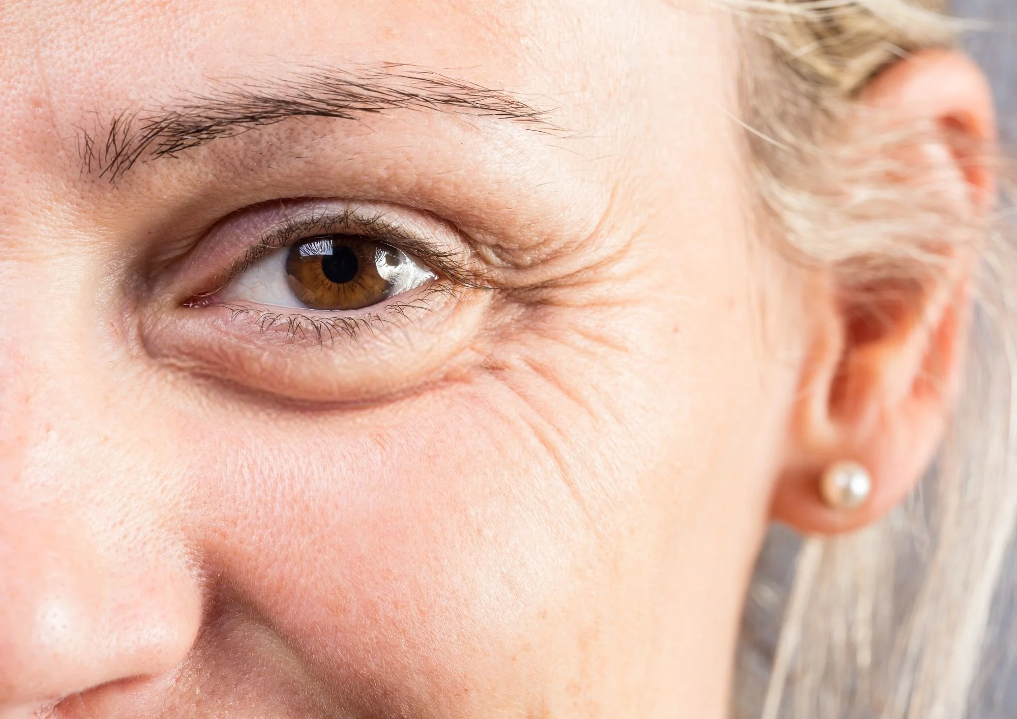 Close-up of a smiling woman's face showing her brown eye, eye wrinkles, and earring.