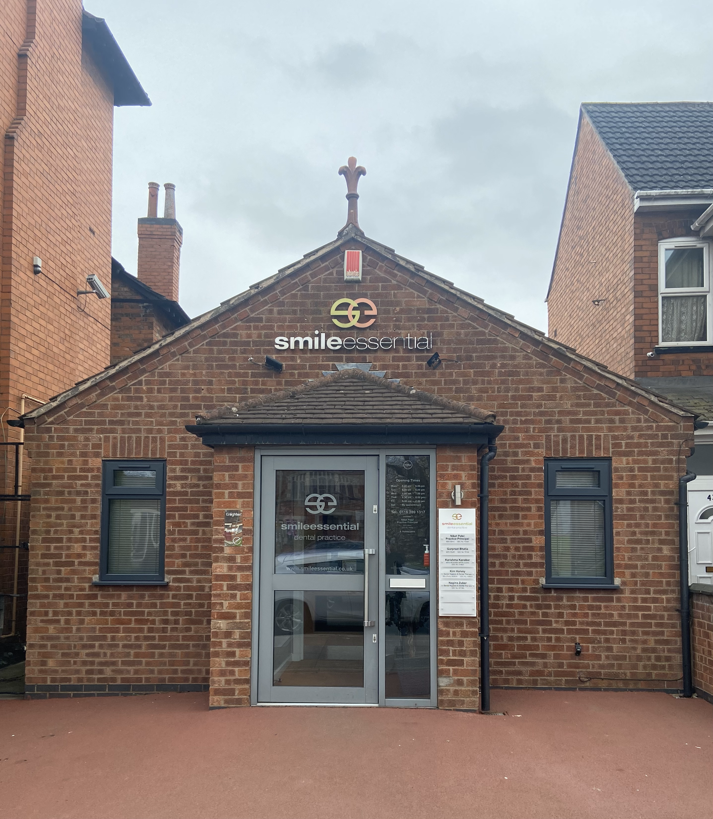 Front view of a small brick dental practice building named Smilee Essential with a glass door, two windows, and signage on the building and door.