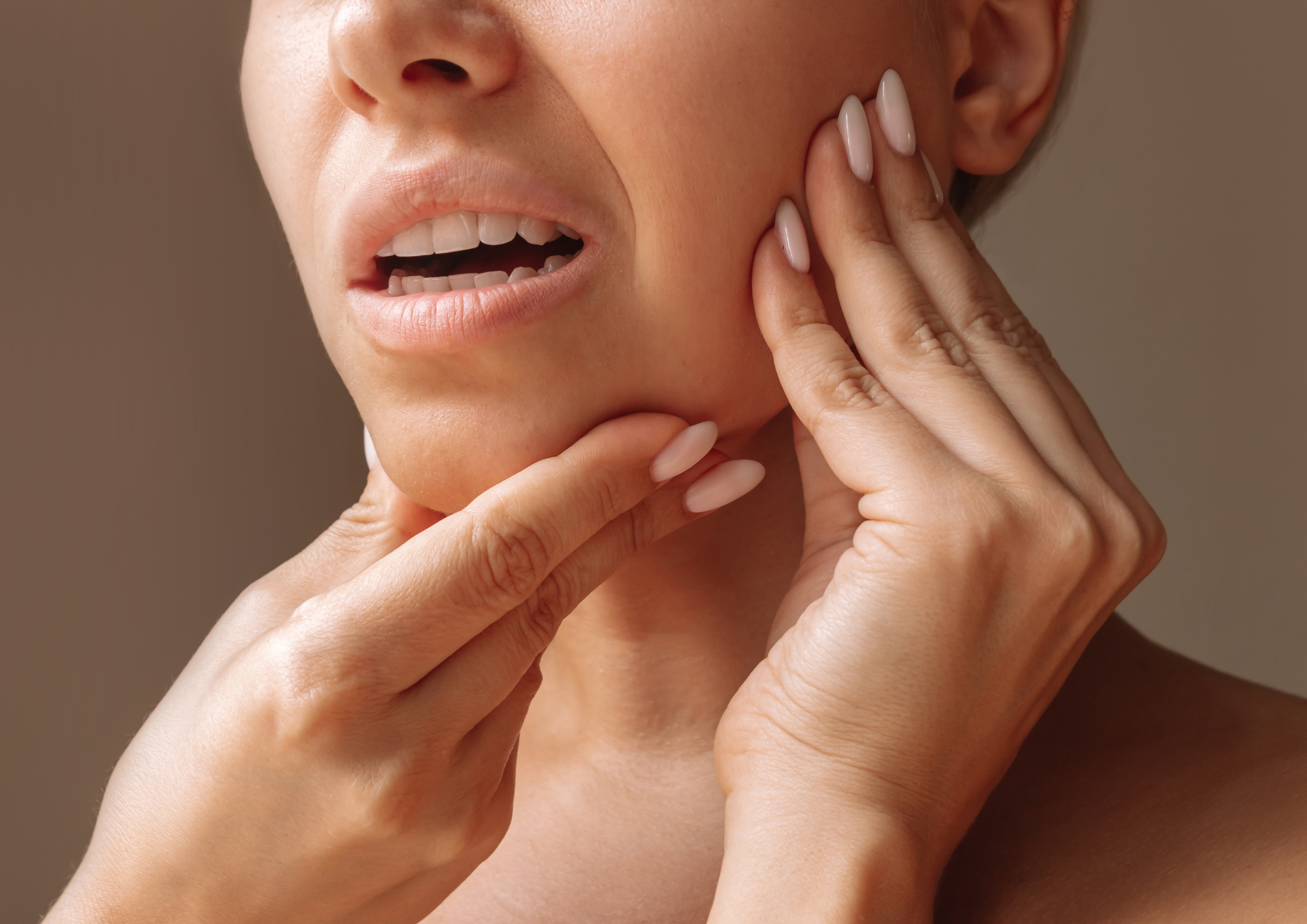 A woman experiencing jaw pain, holding her jaw with her right hand and her chin with her left hand, showing discomfort.
