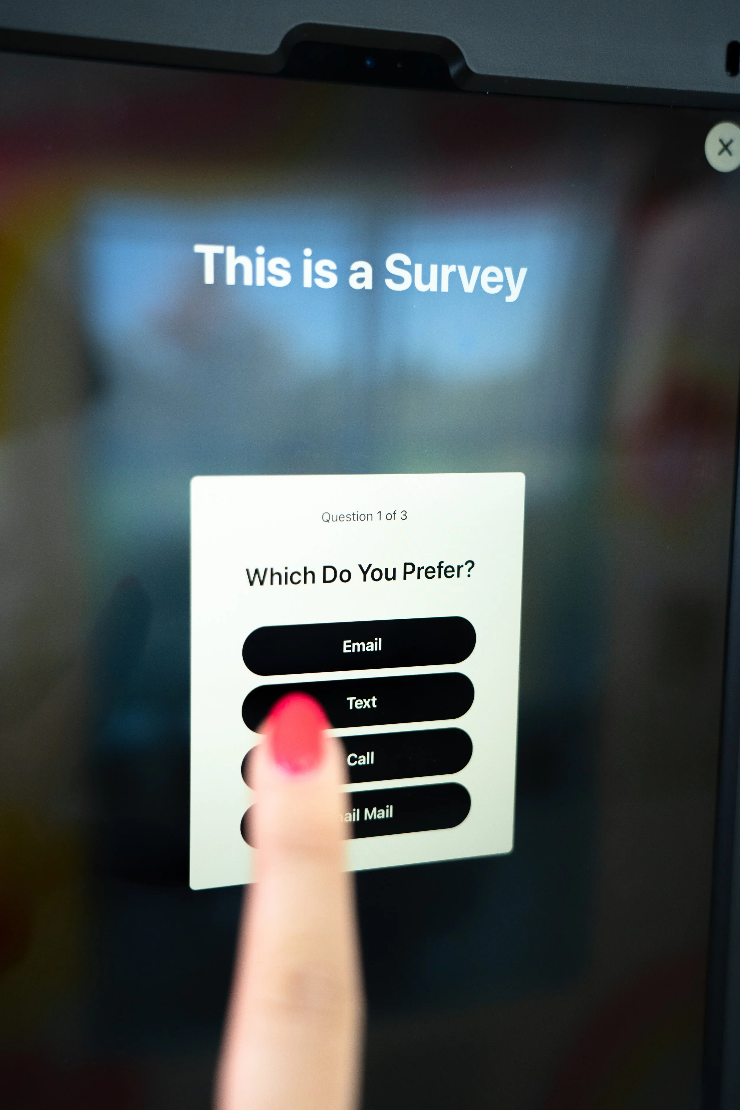 A person with pink painted nails is selecting the 'Text' option on a touchscreen survey interface that asks, 'Which Do You Prefer?' with options Email, Text, Call, and Mail Mail.