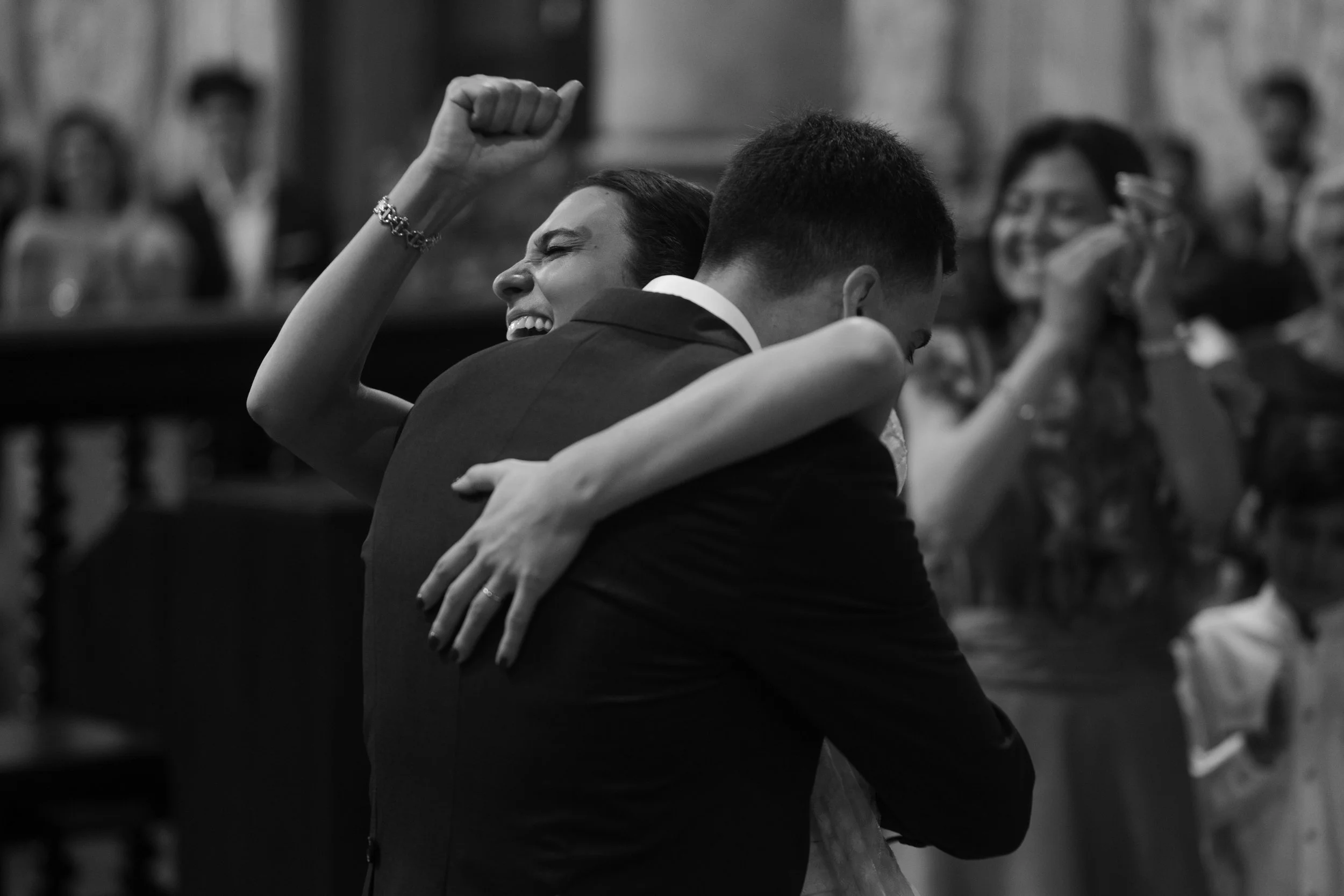 A joyful girl with a bracelet on her wrist and a woman with glasses hugging in a black-and-white photo.
