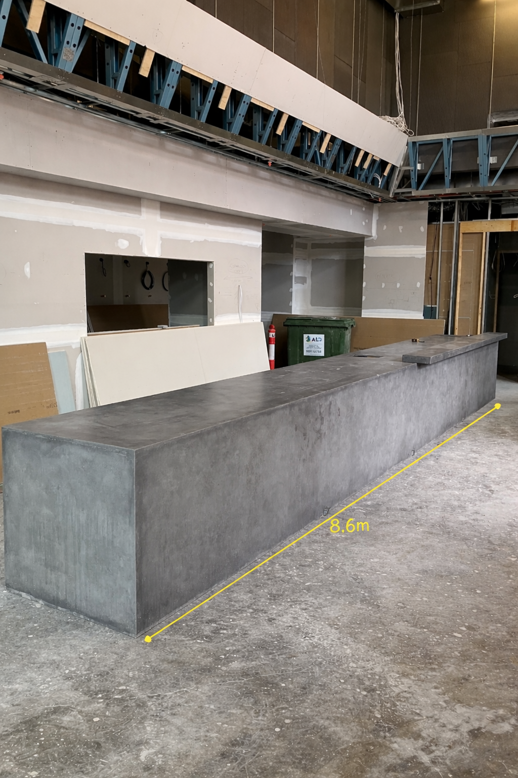 Construction site with a long concrete counter measuring 8.6 meters, unfinished walls, and exposed ceiling framing.