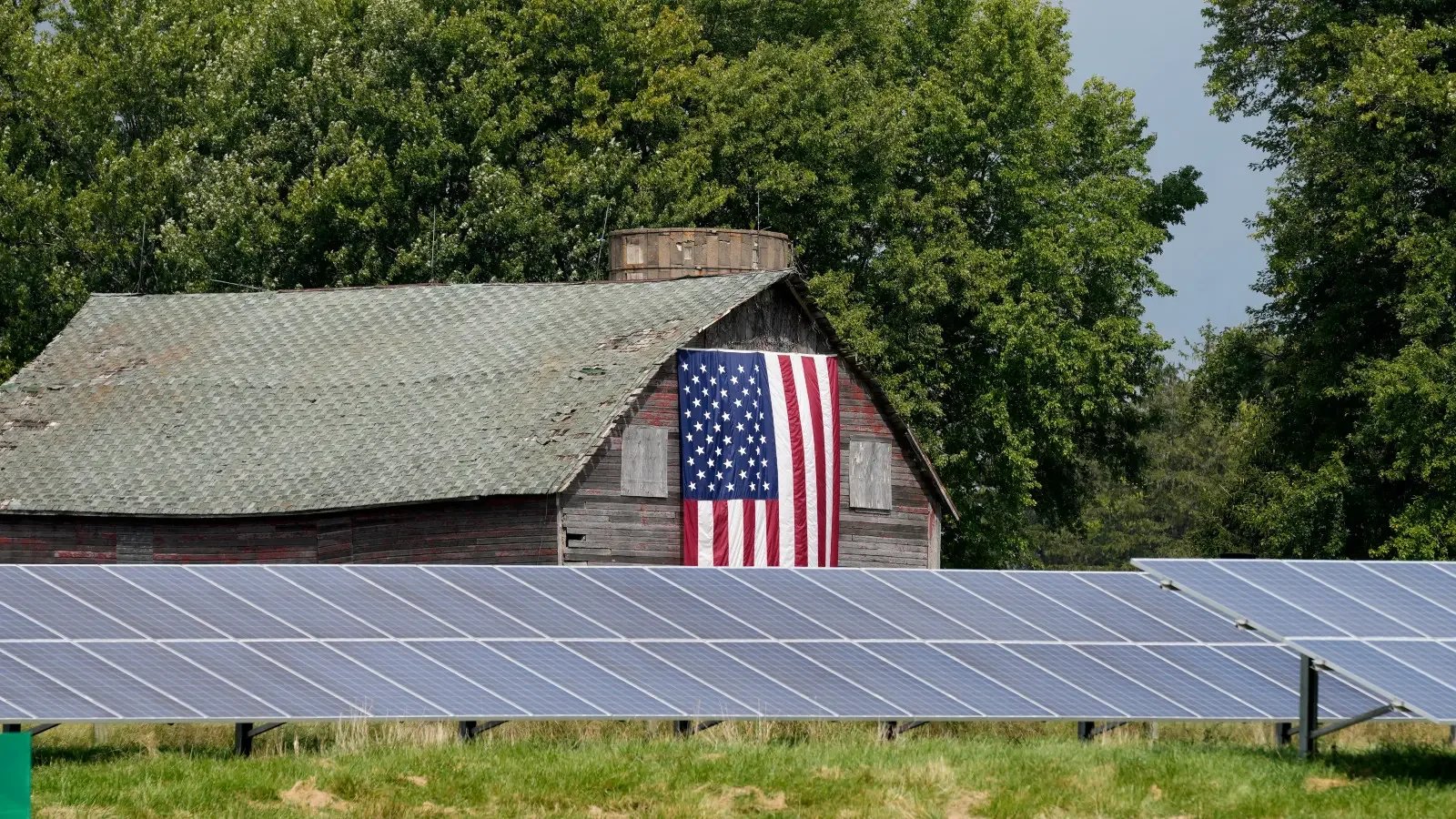Florida Solar panels installed in front of an old wooden barn displaying a large American flag, showcasing rural clean energy adoption in the United States.
