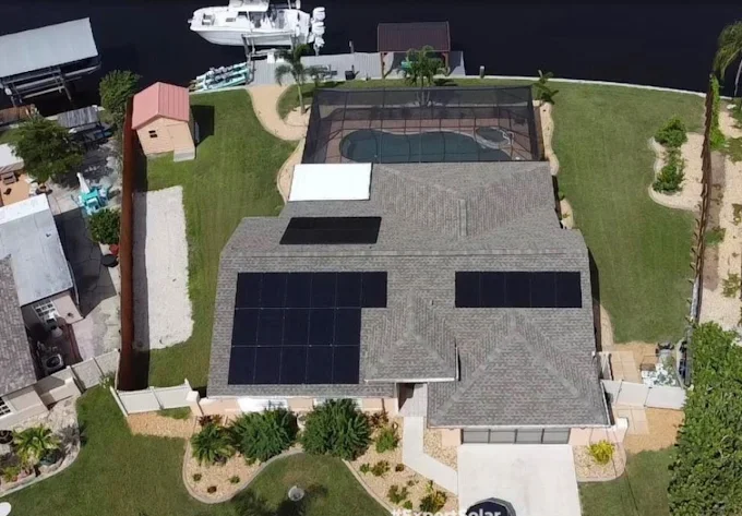Aerial view of a house with solar panels on the roof, a backyard with a tennis court, a small shed outside, and a landscaped yard with grass and plants.