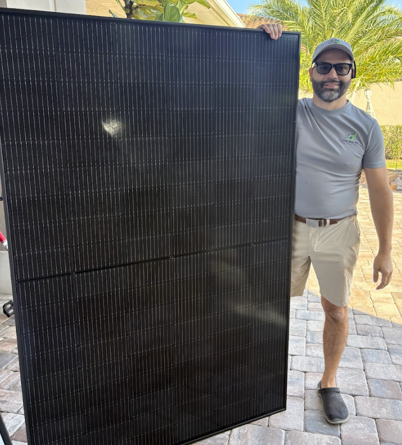 Solar technician standing outdoors holding a large black high-efficiency solar panel during a residential installation in Florida.
