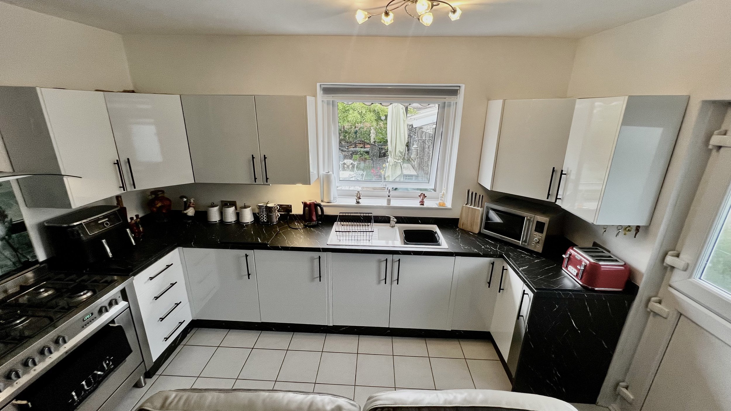 Modern kitchen with white cabinets, black countertops, stove, microwave, toaster, and window.