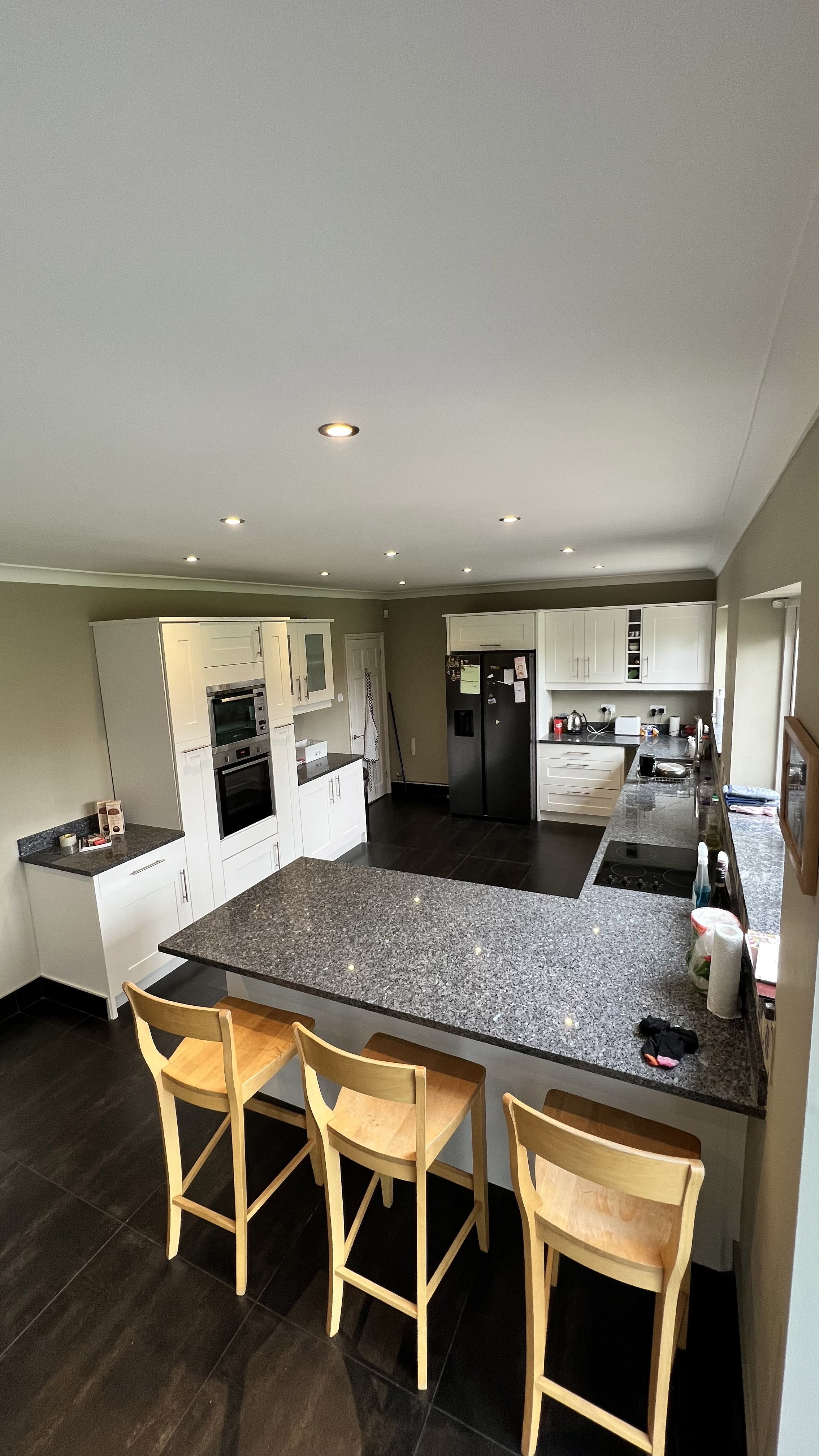Modern kitchen with granite countertops, white cabinets, stainless steel appliances, and wooden bar stools.