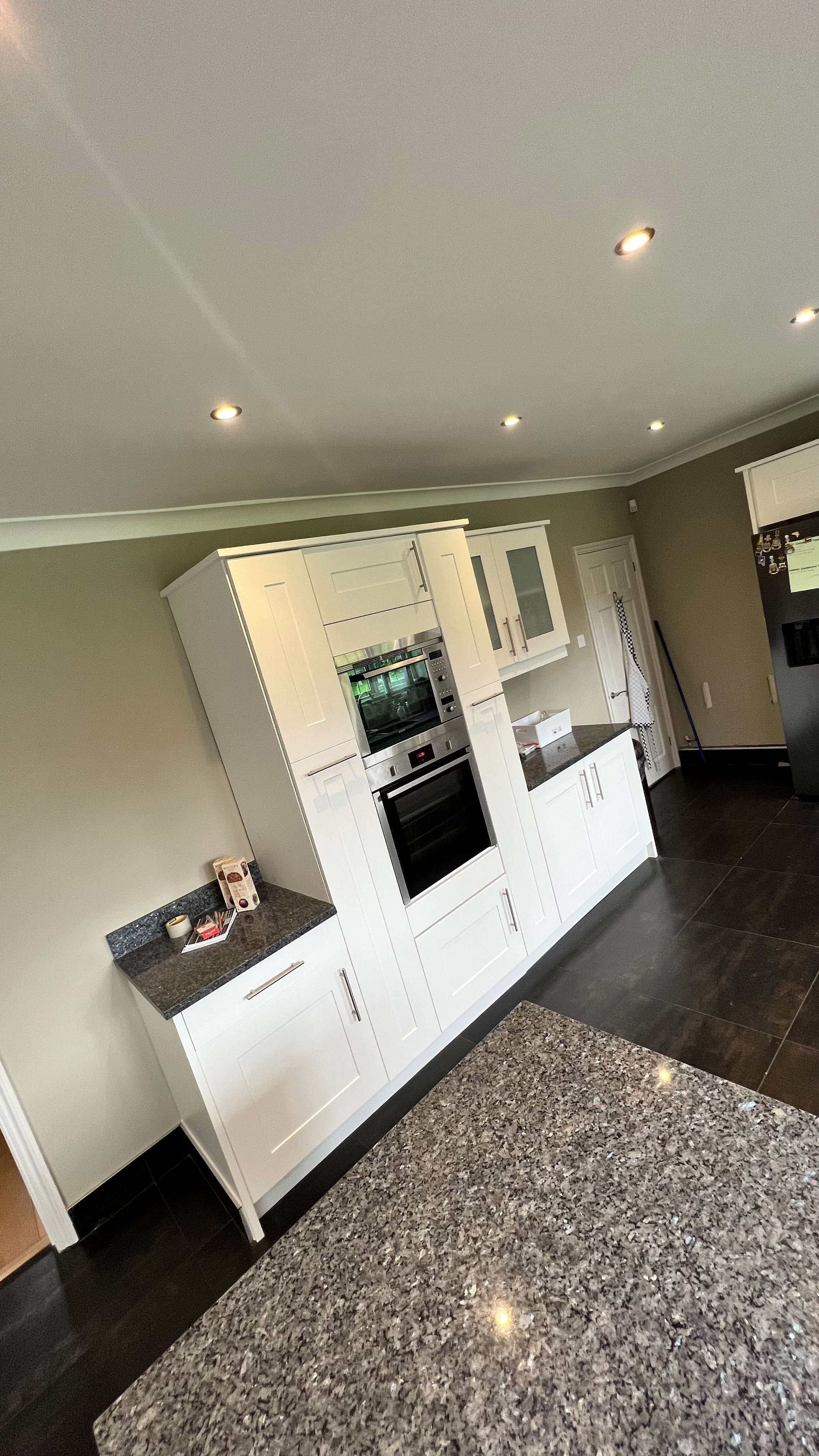 Modern kitchen with white cabinets, granite countertops, built-in oven, and stainless steel appliances.