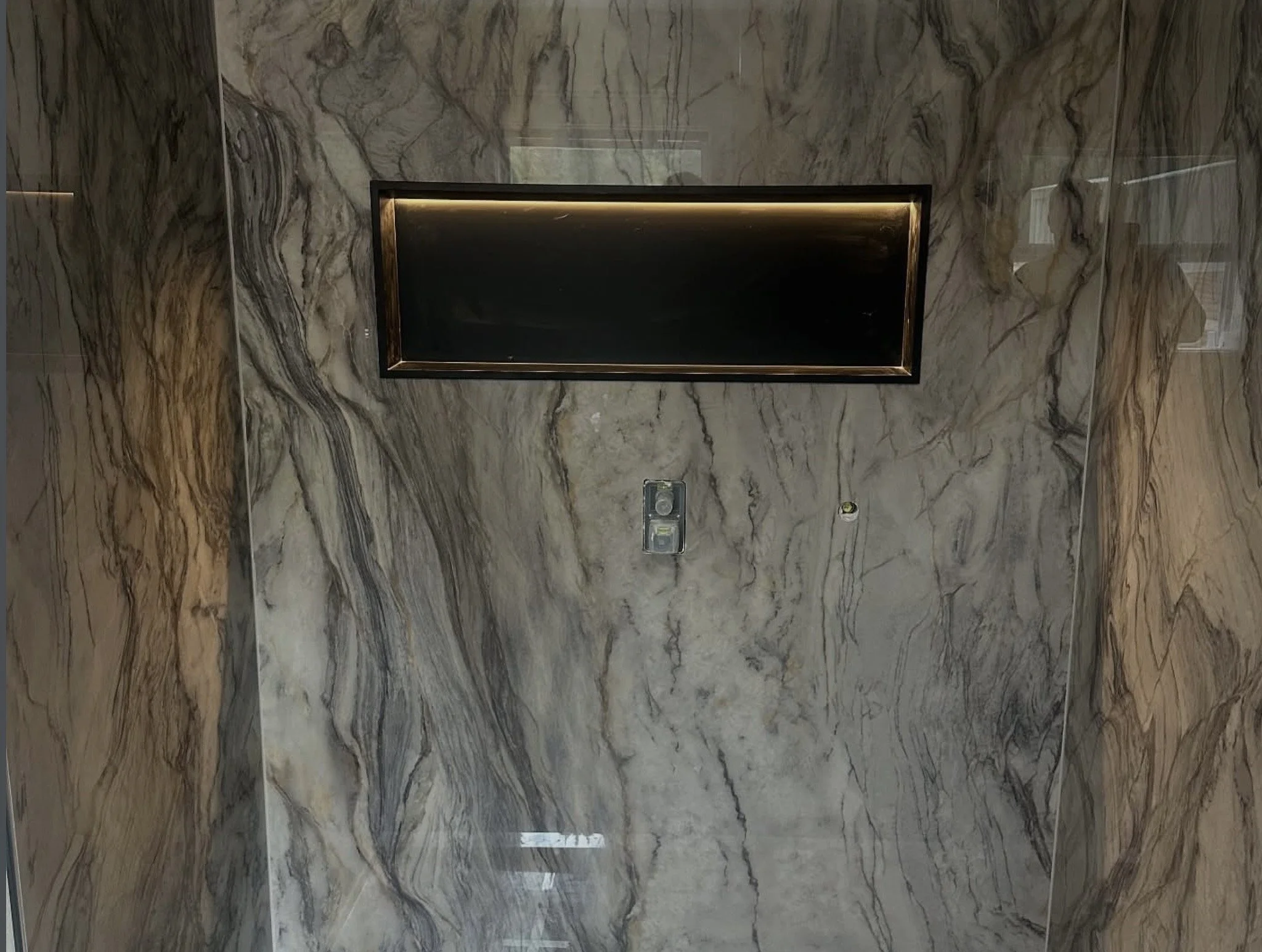 Marble wall with a framed black sign and two small holes, one with an electronic device, possibly a security or sensor system.