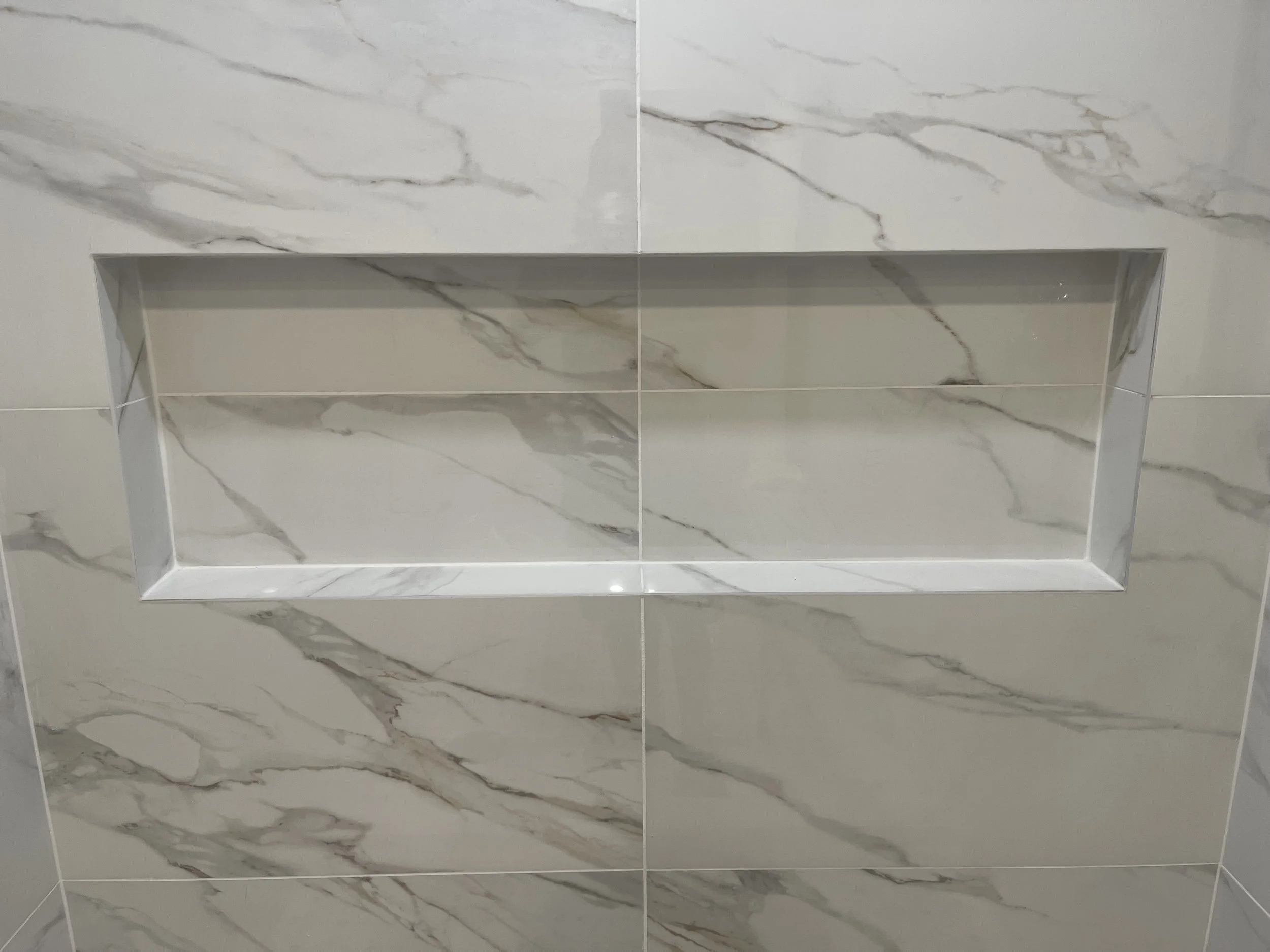 Close-up of a marble tile shower niche with a white marble surface featuring gray and beige veining.