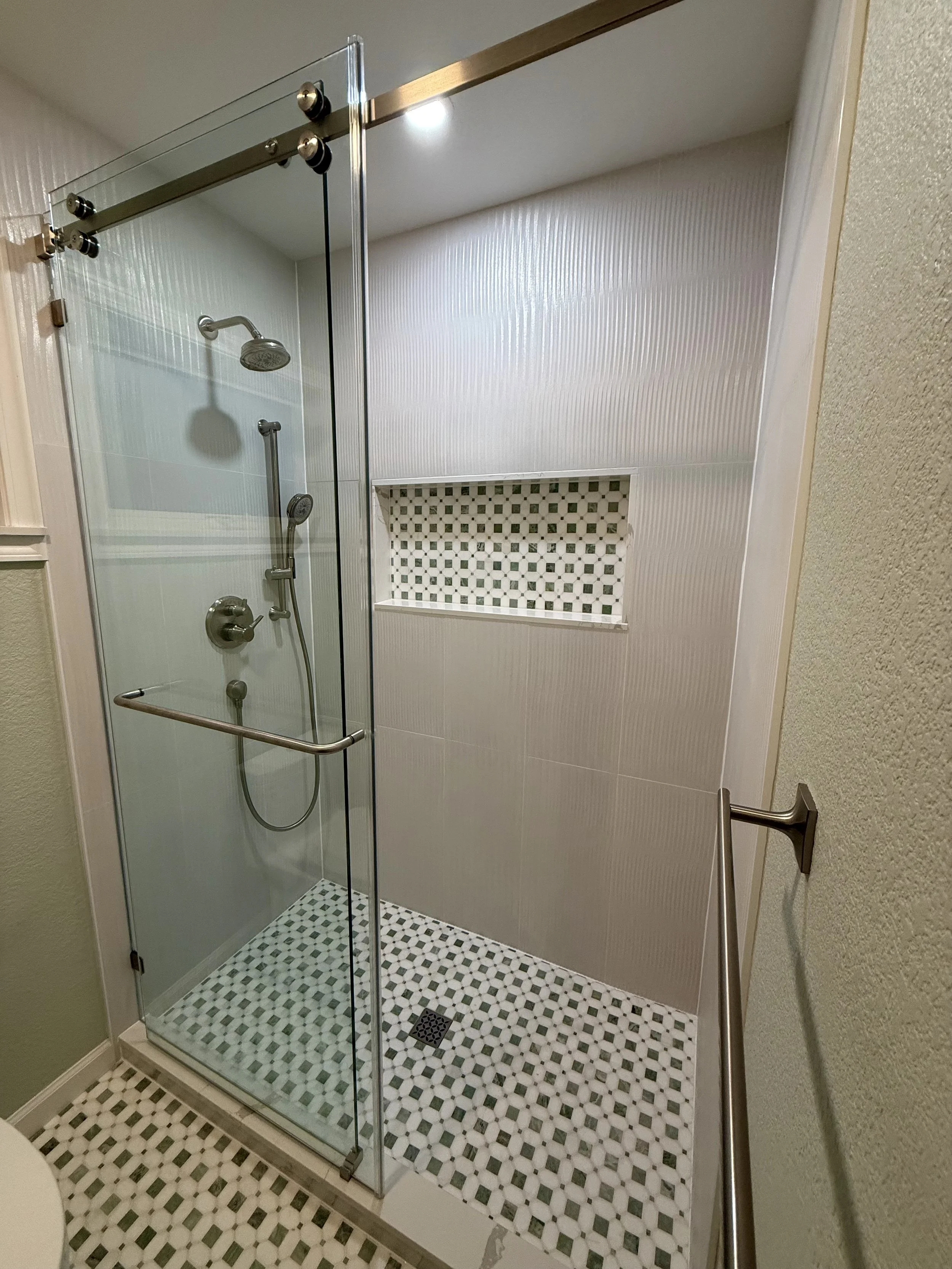 Shower with glass door, tiled walls, built-in niche, and grab bar.