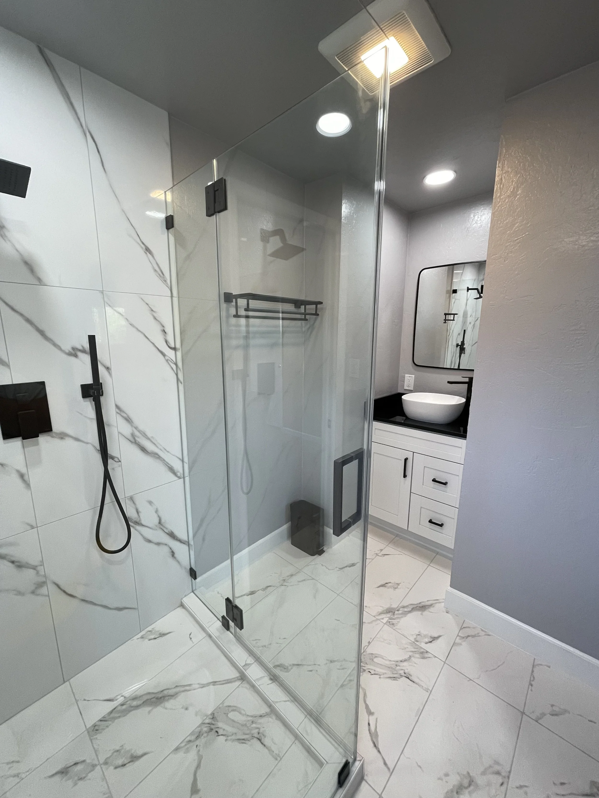 Modern bathroom with marble tile flooring, glass shower enclosure, white vanity with a vessel sink, and a mirror.