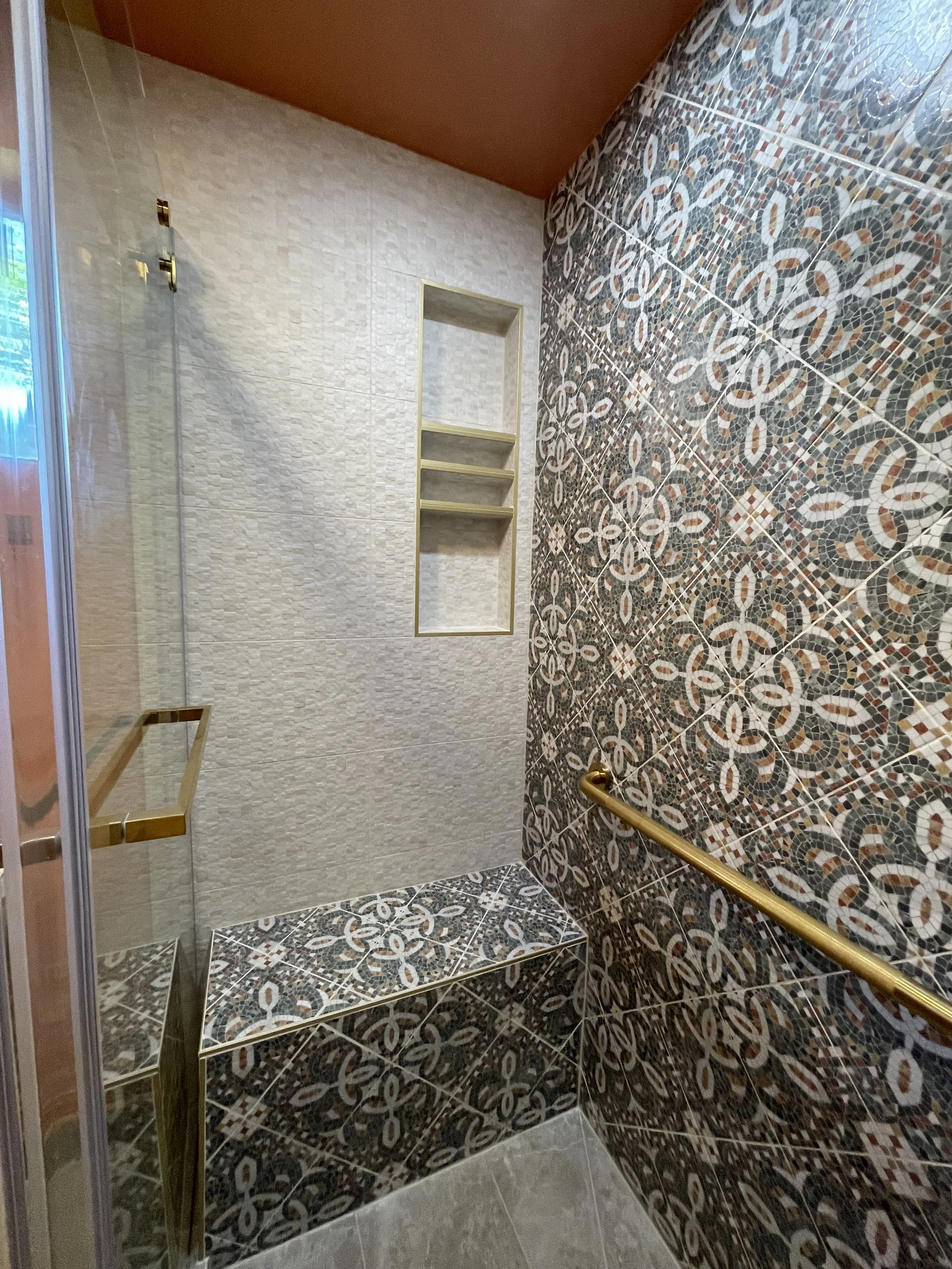 Decorative shower with patterned tiles on the wall and built-in shelves.