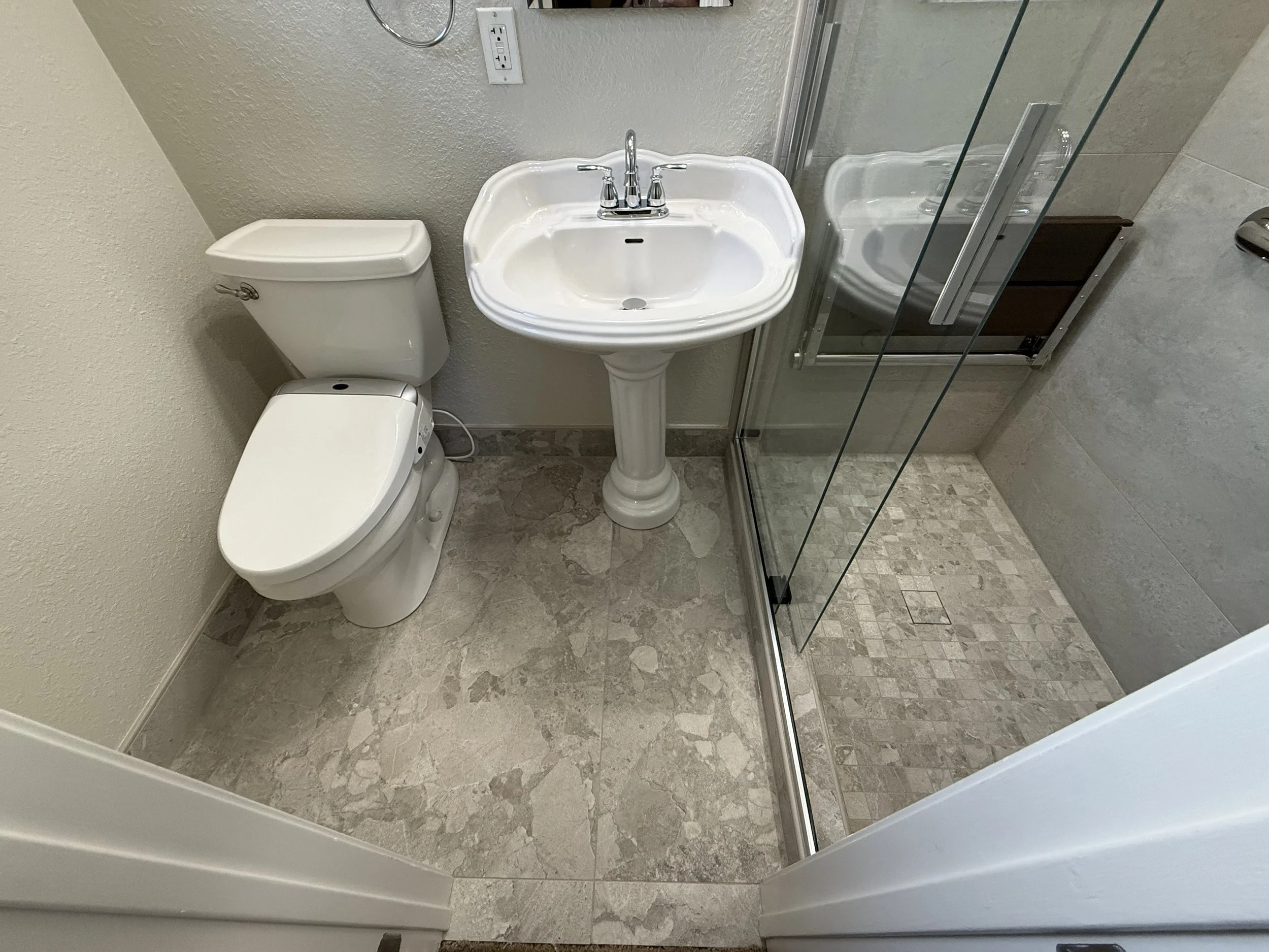 A small bathroom with a toilet, a pedestal sink, and a glass shower stall with a tiled shower floor.